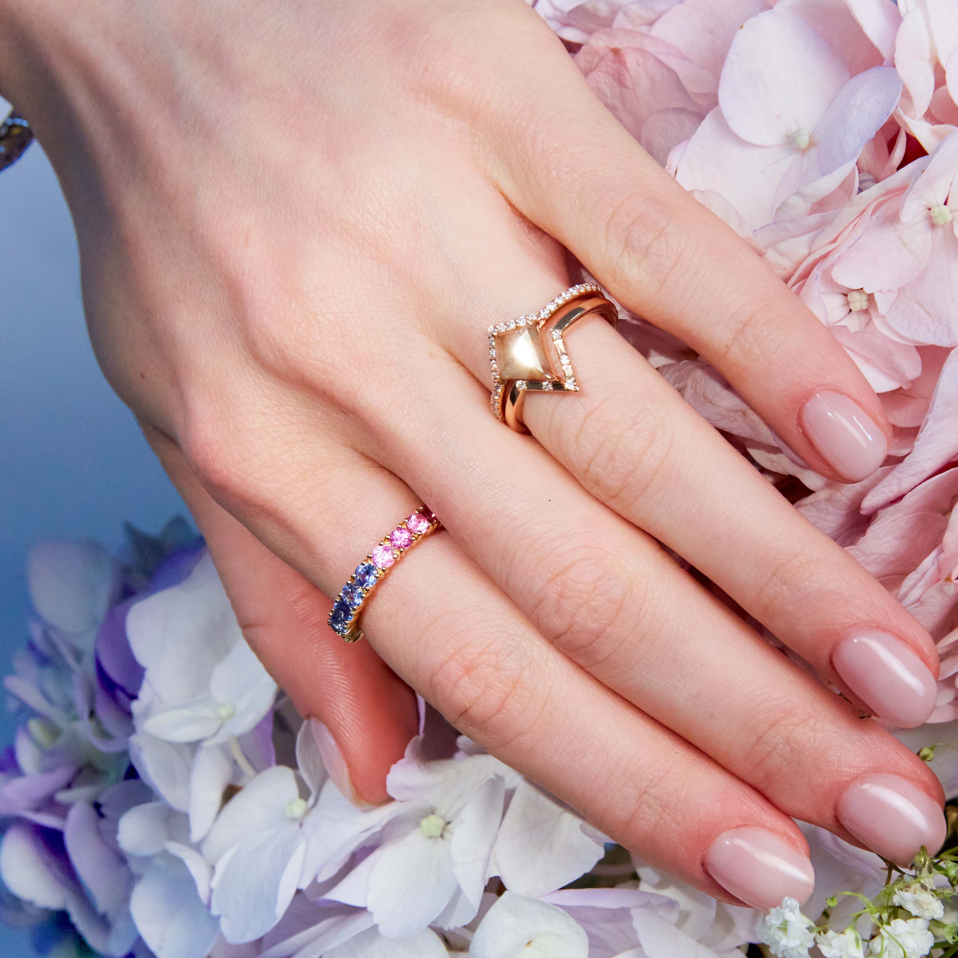 Penta band, Salt and pepper diamond ring two and an eternity rainbow sapphire band on hand surrounded by pink flowers