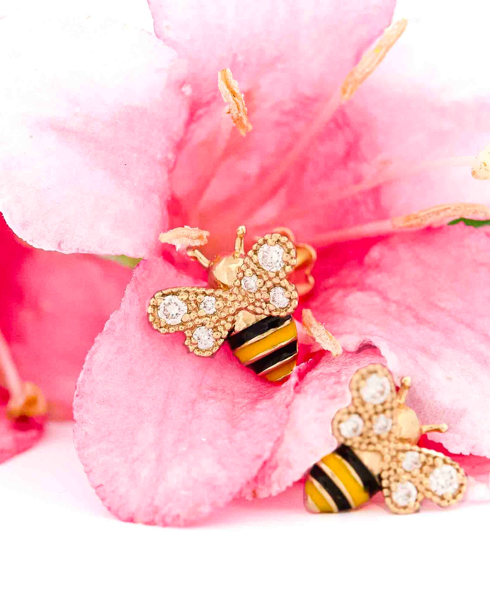 Yellow Gold bee-shaped earrings with black and yellow enamel details and diamonds on wings on pink floral background