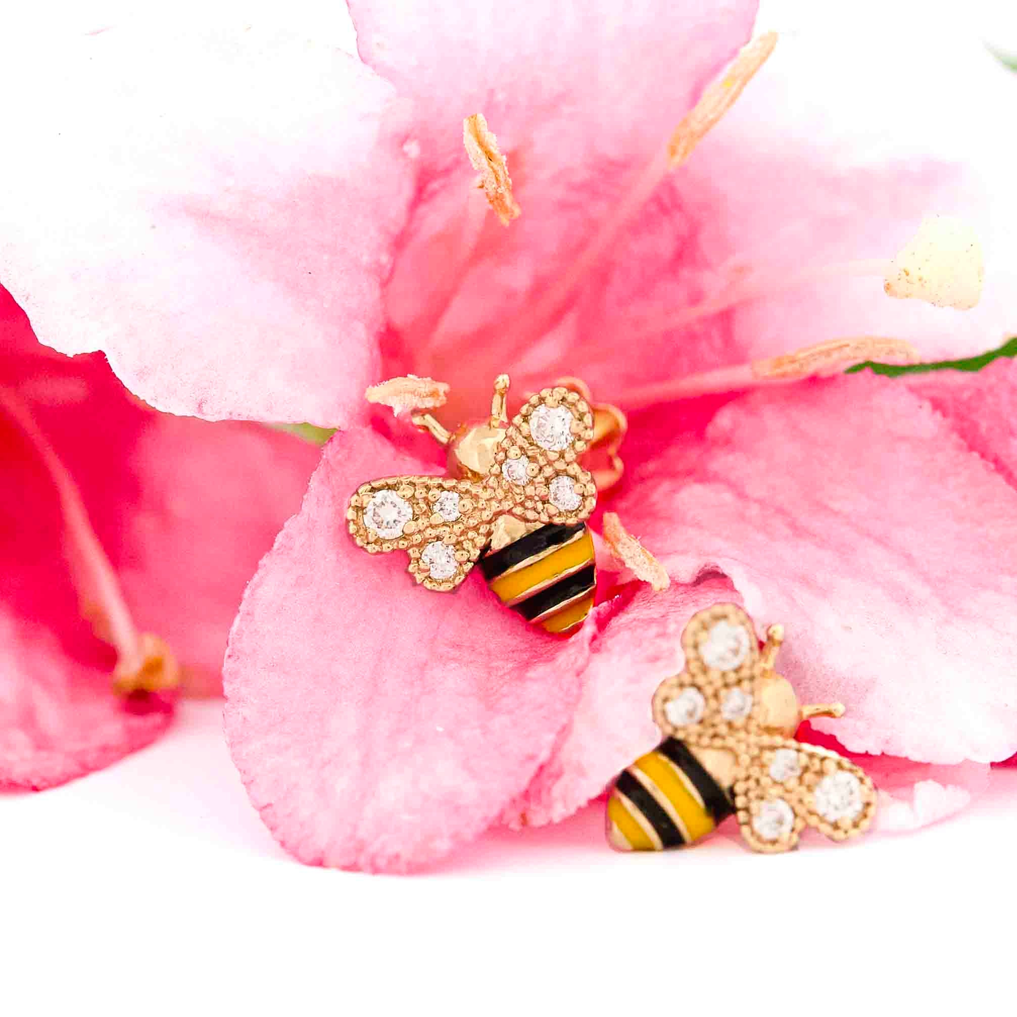 Yellow Gold bee-shaped earrings with black and yellow enamel details and diamonds on wings on pink floral background