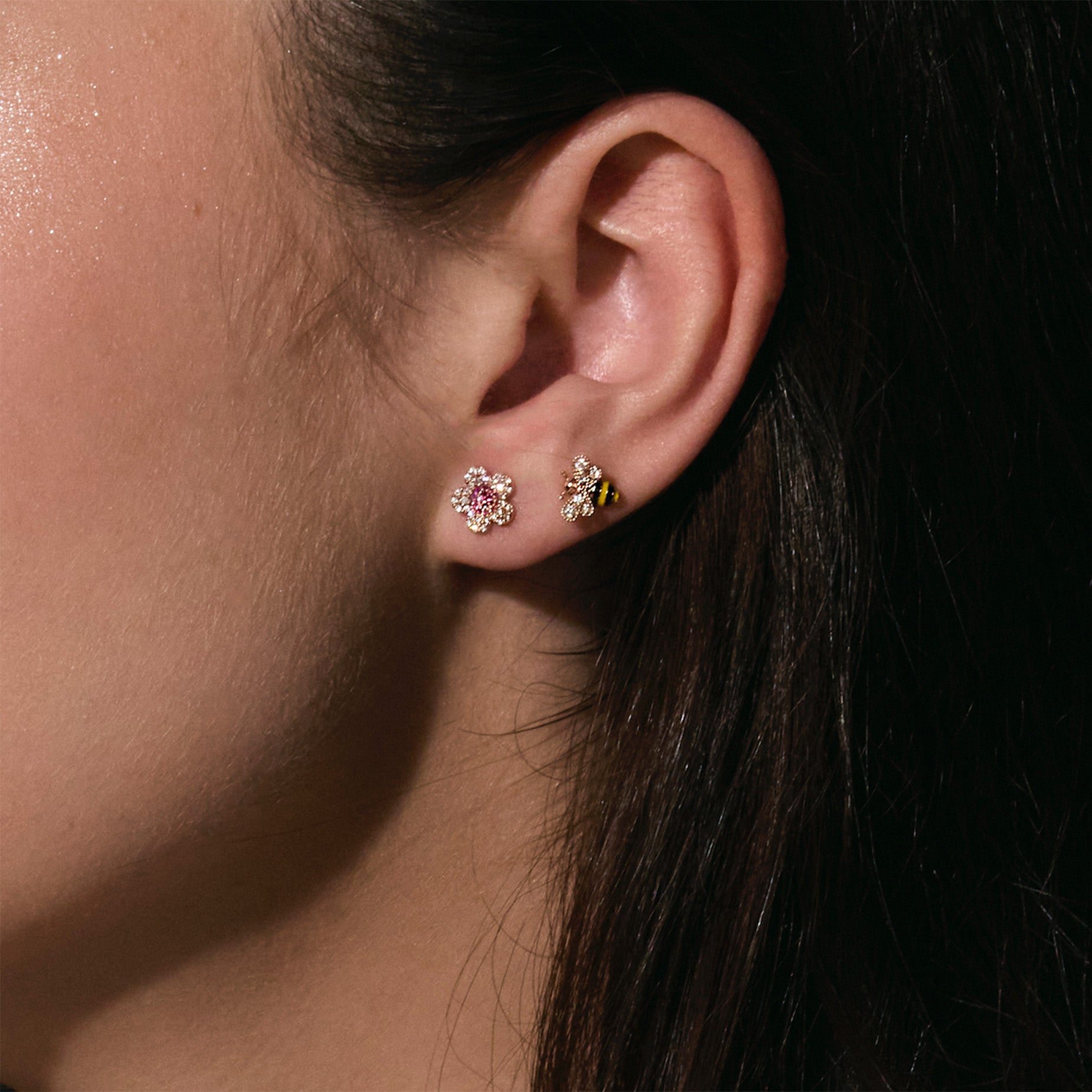 Close-up of an ear wearing two earrings , one is a gold bee with enamel black and yellow stripes and the other one is a diamonds and rubies cherry blossom flower