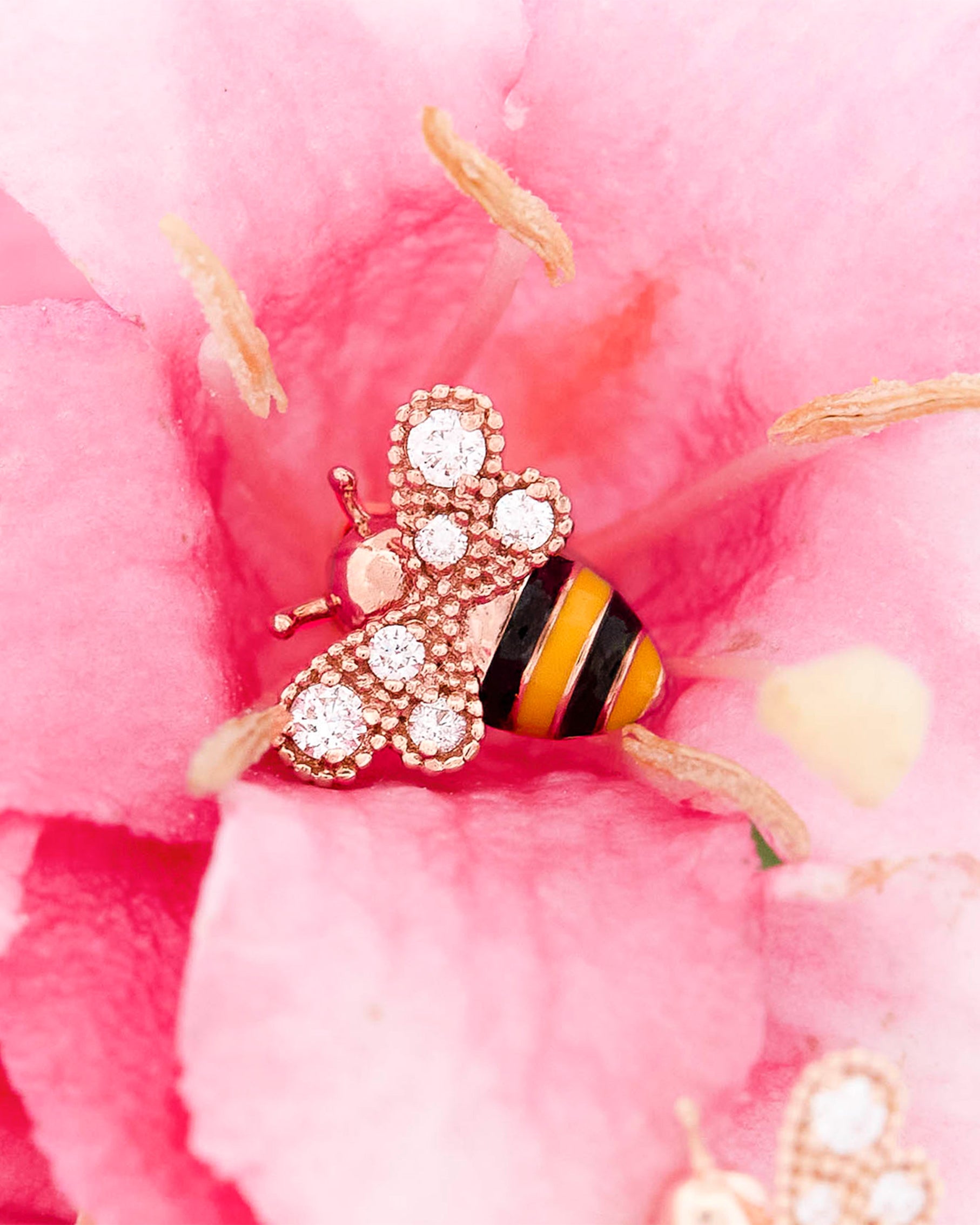 Rose Gold bee-shaped earrings with black and yellow enamel and round diamonds on wings stripes on a oink flower background