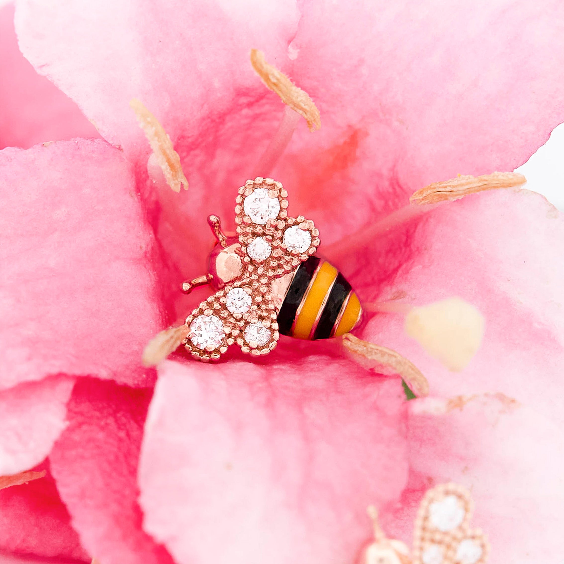Rose Gold bee-shaped earrings with black and yellow enamel and round diamonds on wings stripes on a oink flower background