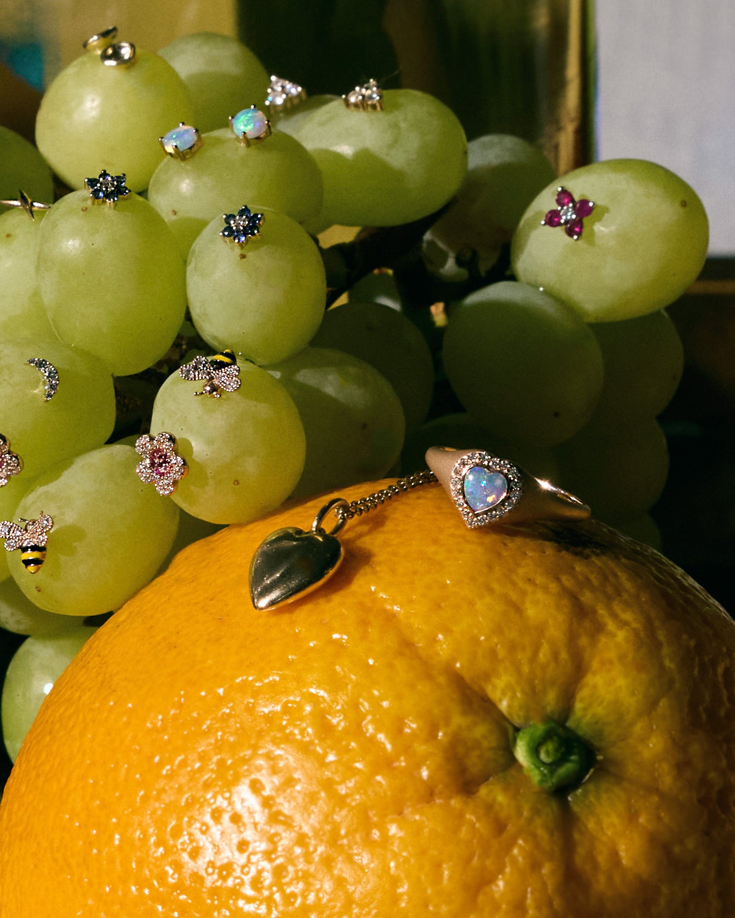 Close-up of green grapes full of earrings and an orange with jewelry on it on a dark background
