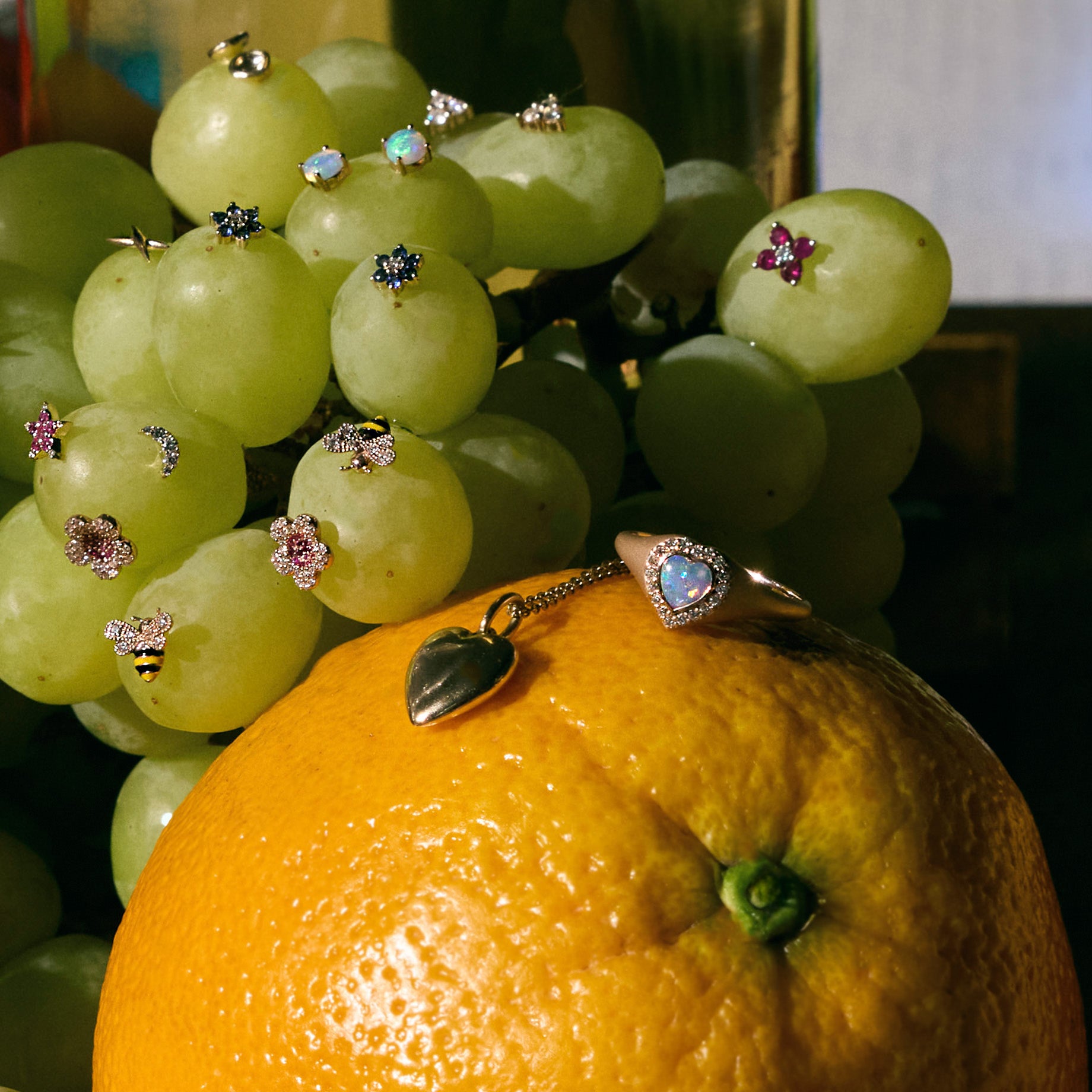 Close-up of green grapes full of earrings and an orange with jewelry on it on a dark background