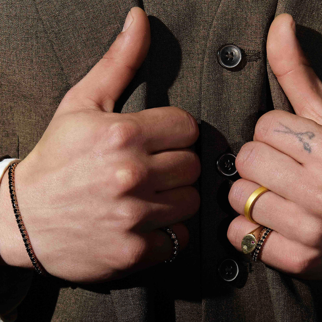 Close-up of hands buttoning a jacket with a focus on details like bracelets and rings.