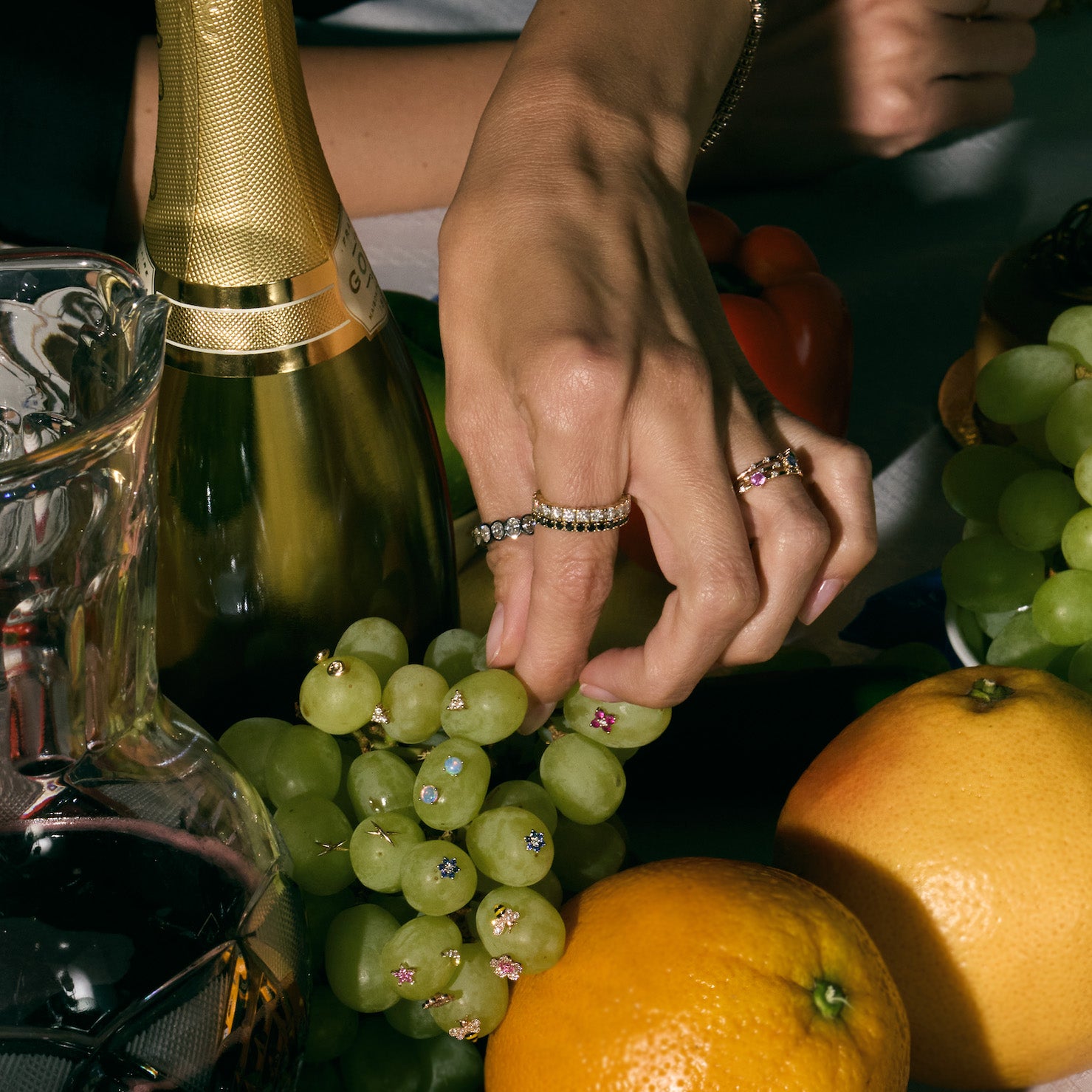 Hand picking a grape from a vine full of earrings, wearing beautiful rings