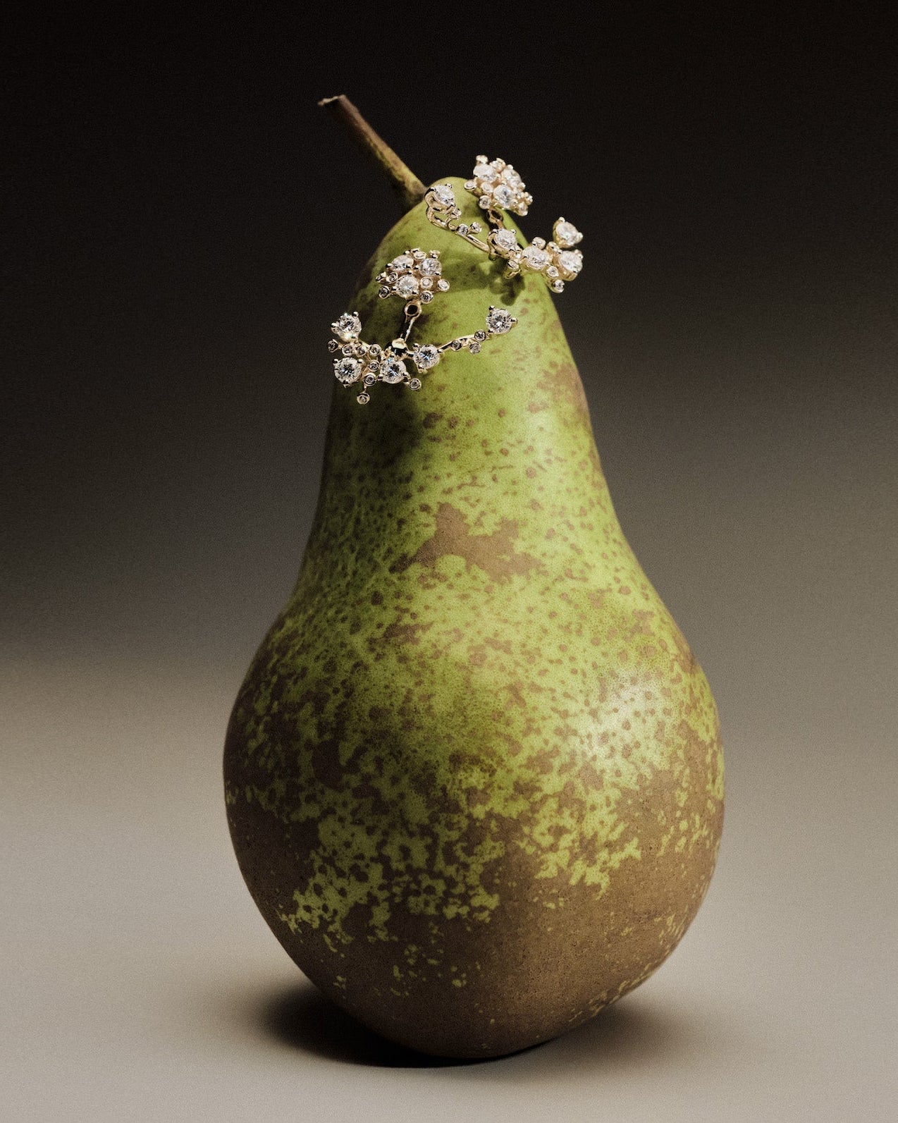 Gold and diamond earrings on a green pear against a dark background.