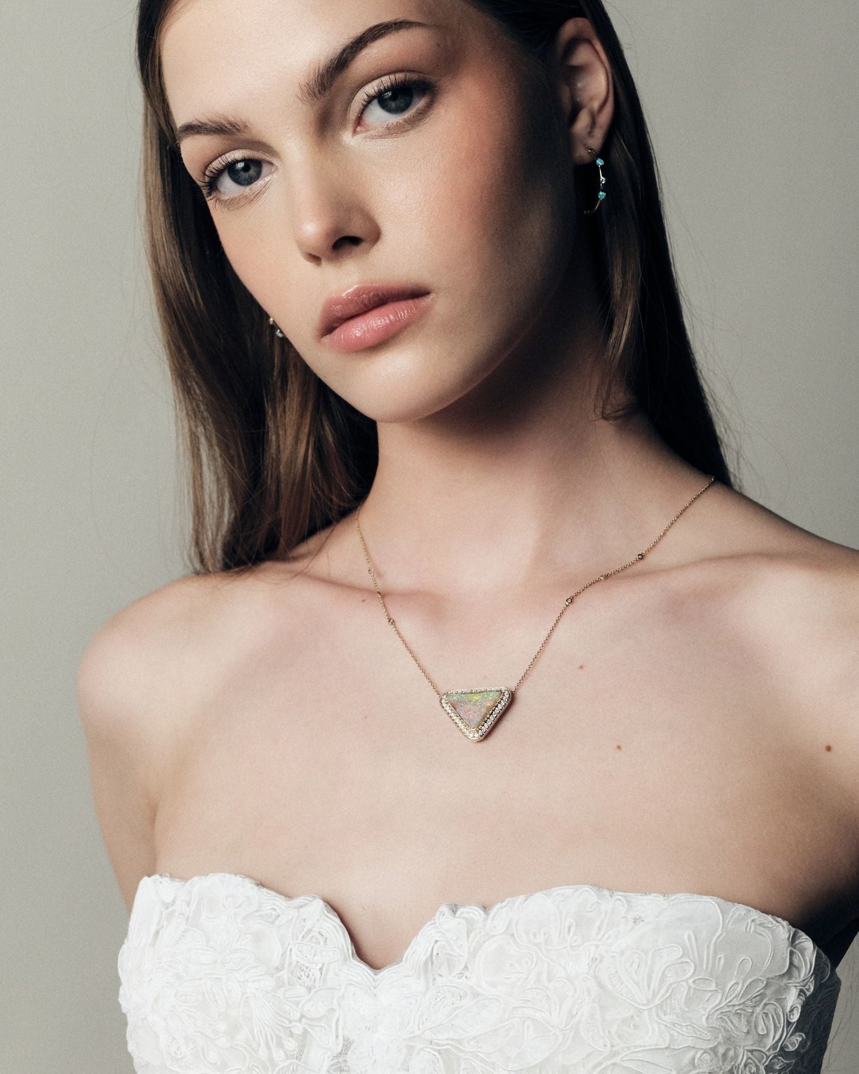 Woman wearing a white strapless dress and a gold necklace with diamonds and a trillion Australian Opal Boulder pendant against a plain background