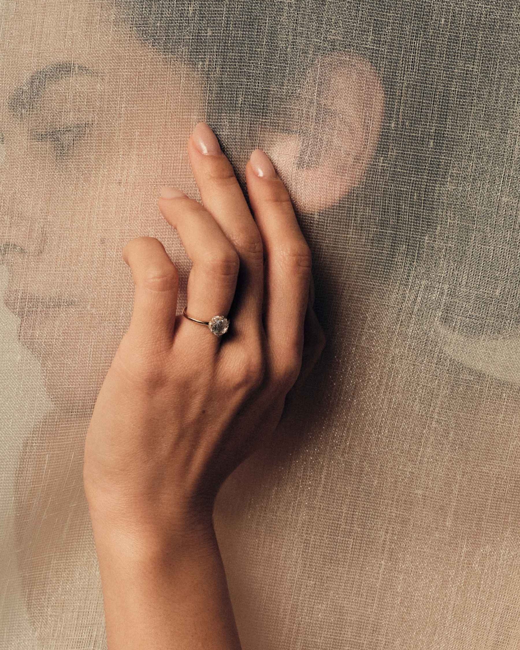 Hand wearing a rose cut diamond ring on a textured beige background.
