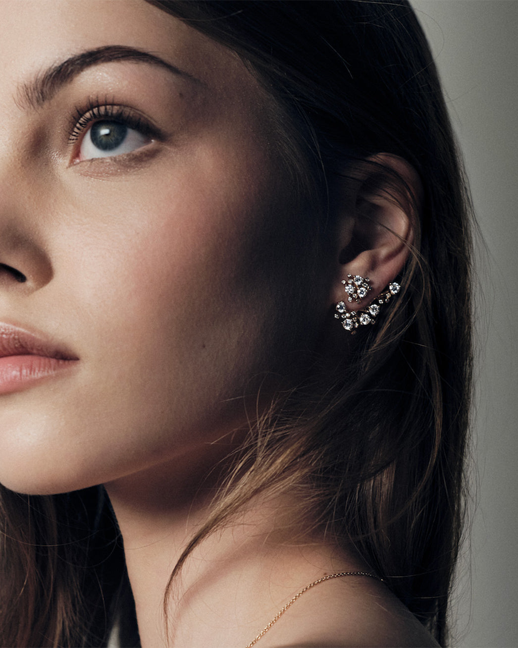 Close-up of a woman wearing a delicate bloom gold and diamonds earring with a neutral background