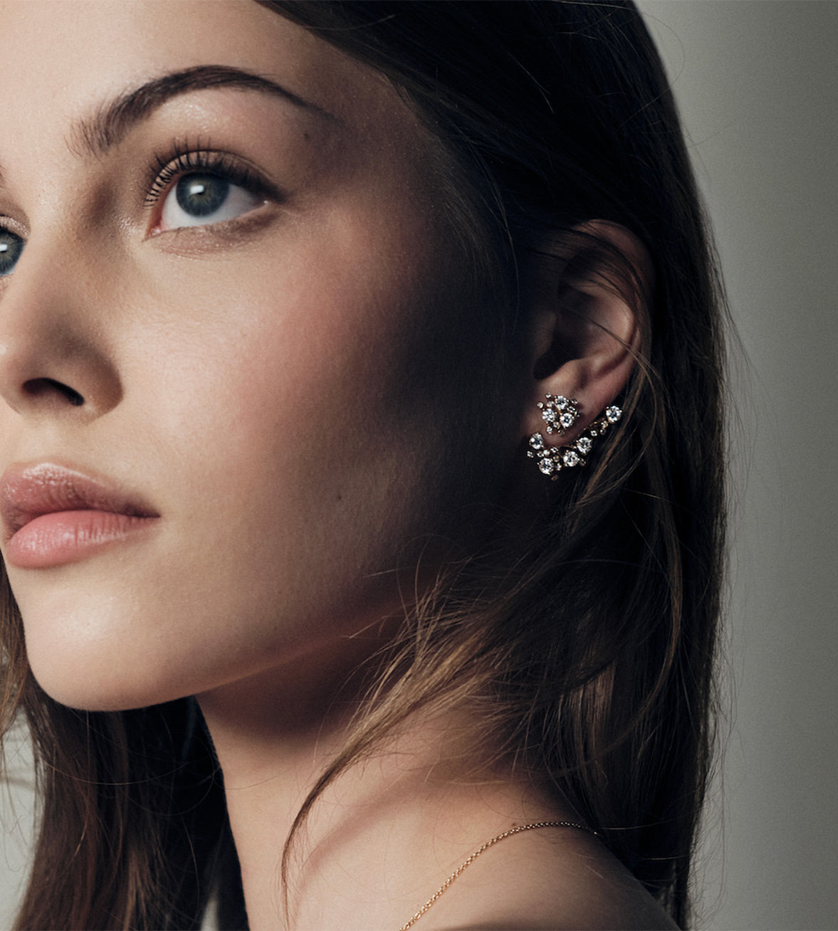 Close-up of a woman wearing a delicate bloom gold and diamonds earring with a neutral background