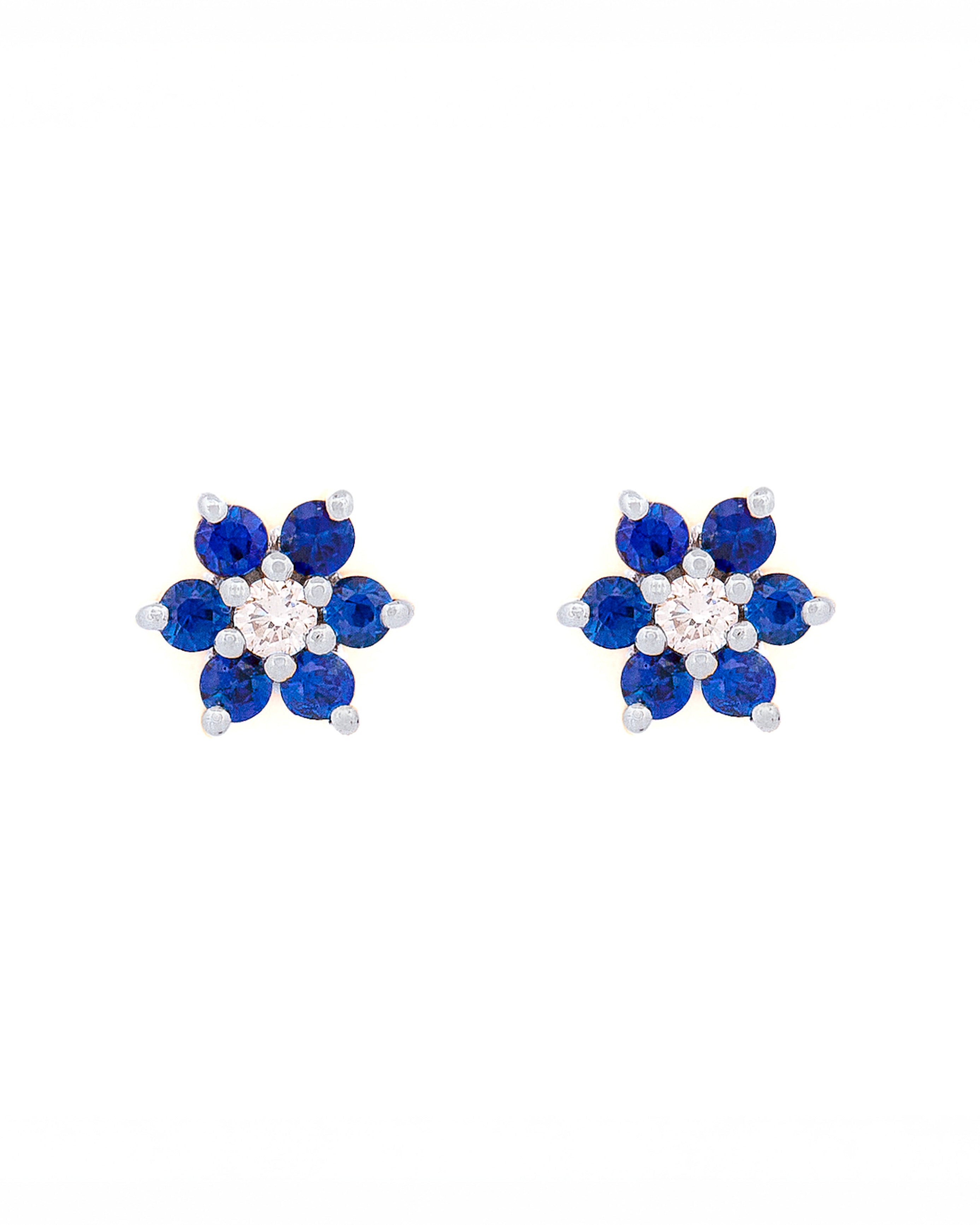 Pair of floral earrings with blue sapphires and diamonds and white gold accents on a white background