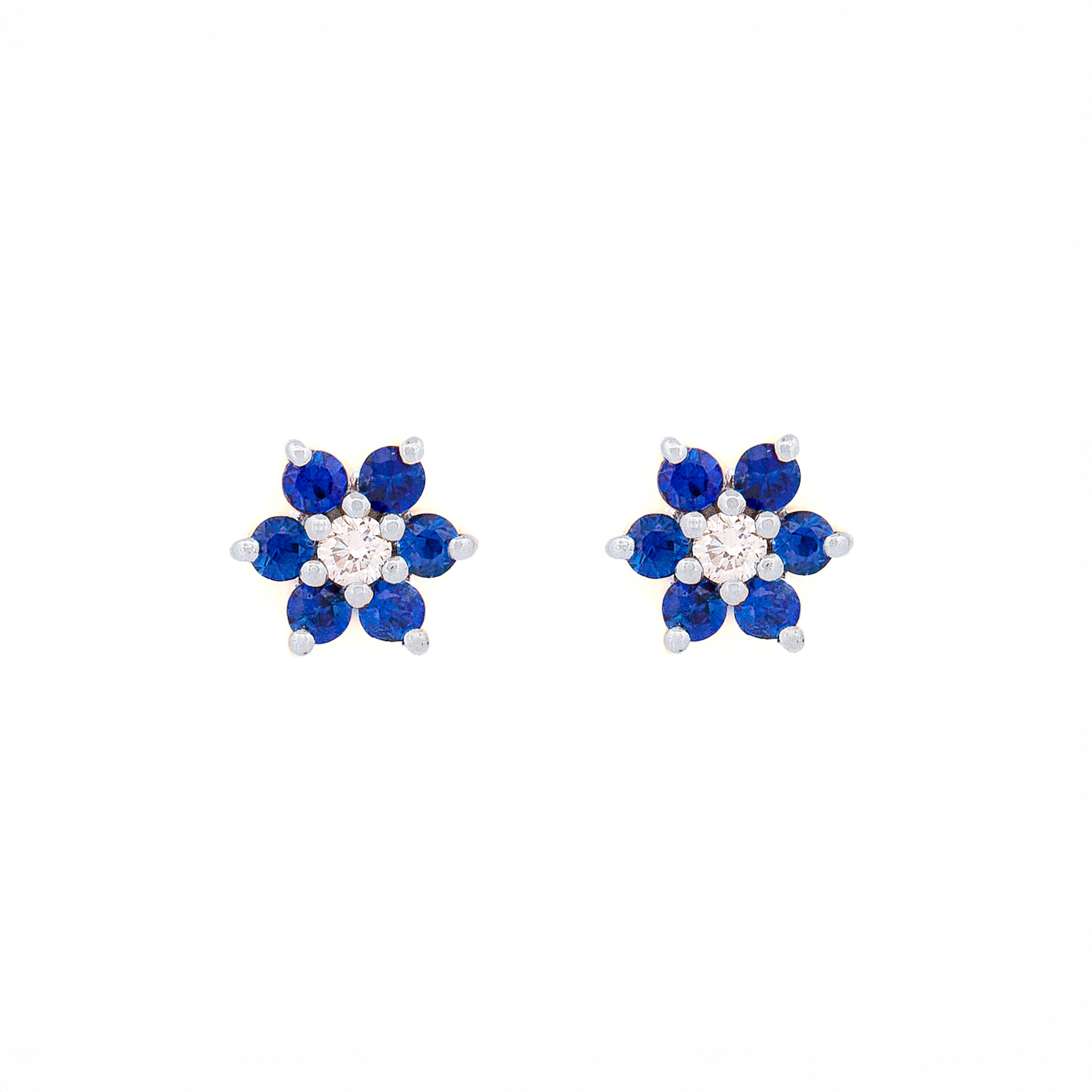 Pair of floral earrings with blue sapphires and diamonds and white gold accents on a white background