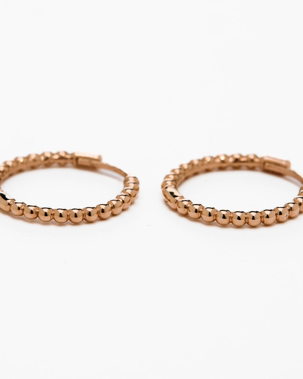 A pair of rose gold-colored hoop earrings with a textured surface, displayed against a white background.