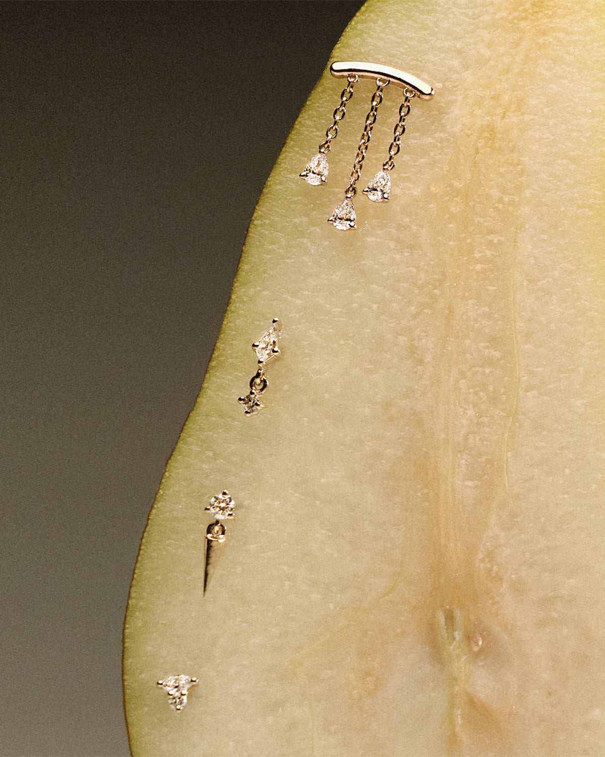 Gold earrings, teardrop diamonds chandelier stud, The Floating Kite Diamond Stud, The Floating Gold Icicle Stud, The Marquise and Round Diamond stud, on a pear with a neutral backgrounda.
