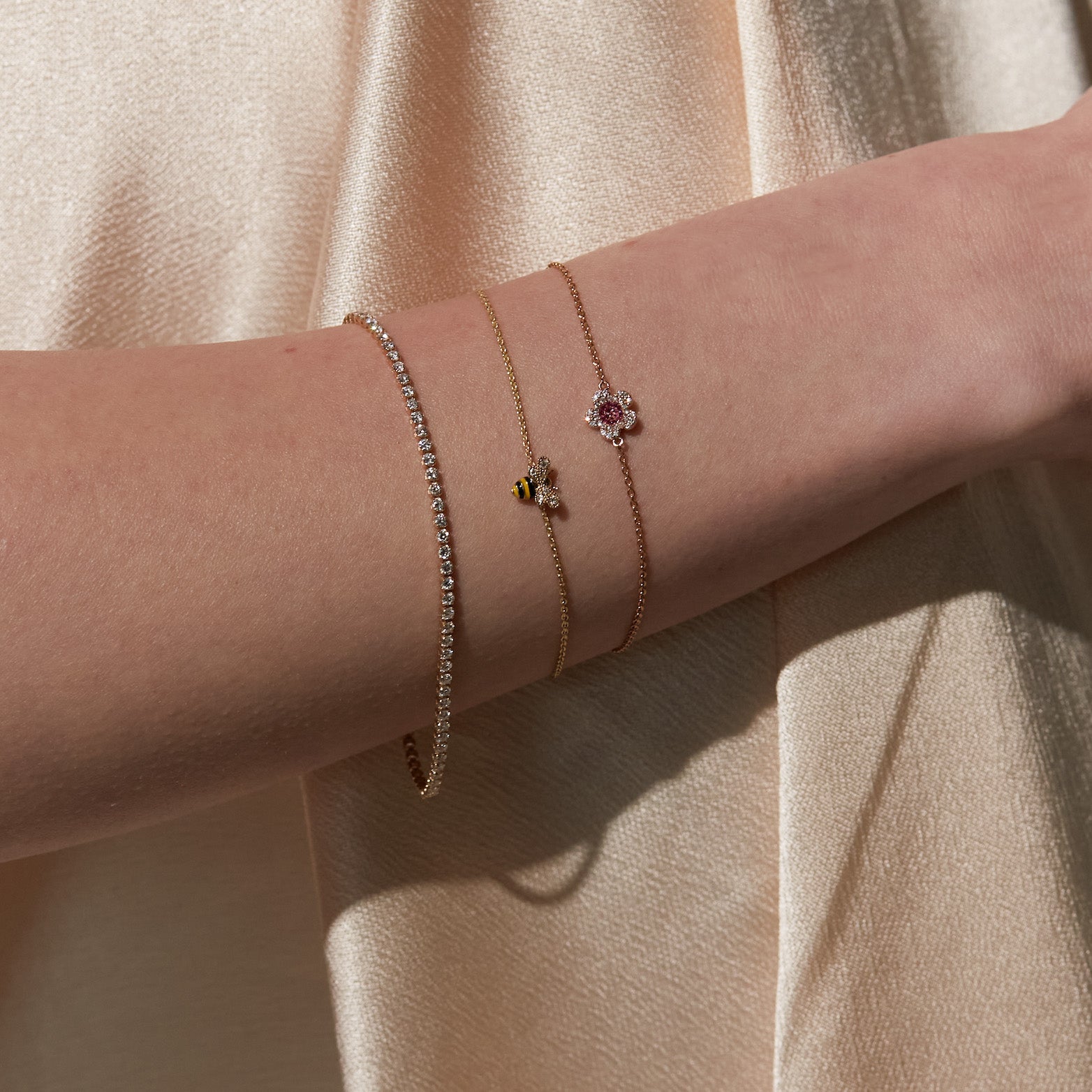 Close-up of a person's arm wearing three delicate bracelets on a beige background