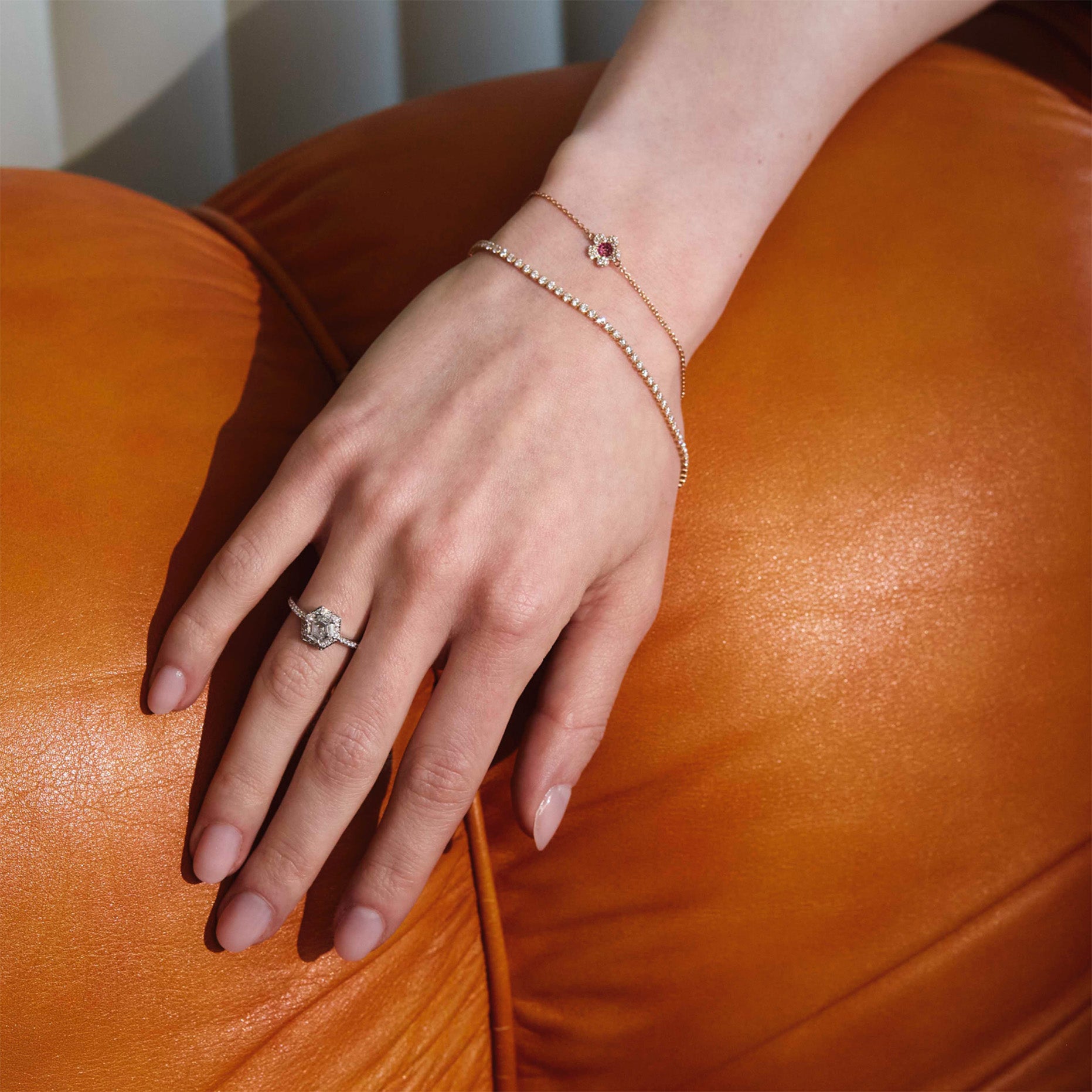 Hand wearing a ring, tennis bracelet, cherry blossom flower diamonds bracelet, on an orange leather surface
