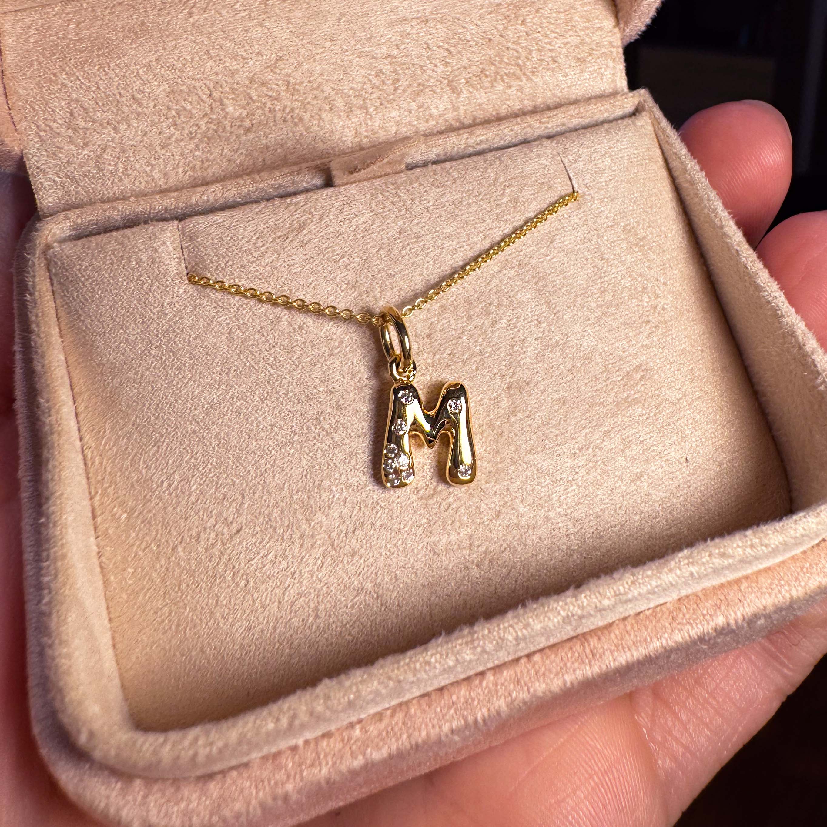 Gold and diamonds necklace with a 'M' pendant in a jewelry box