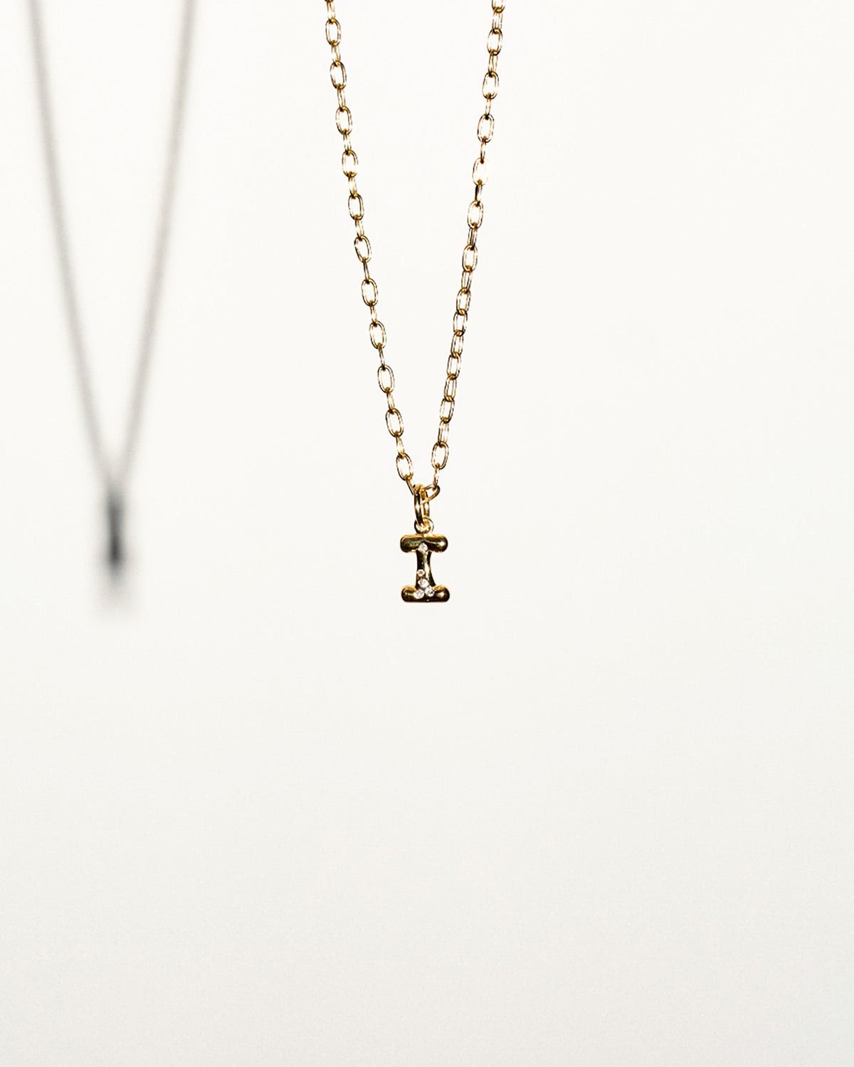 Gold necklace with a small I letter pendant on a white background