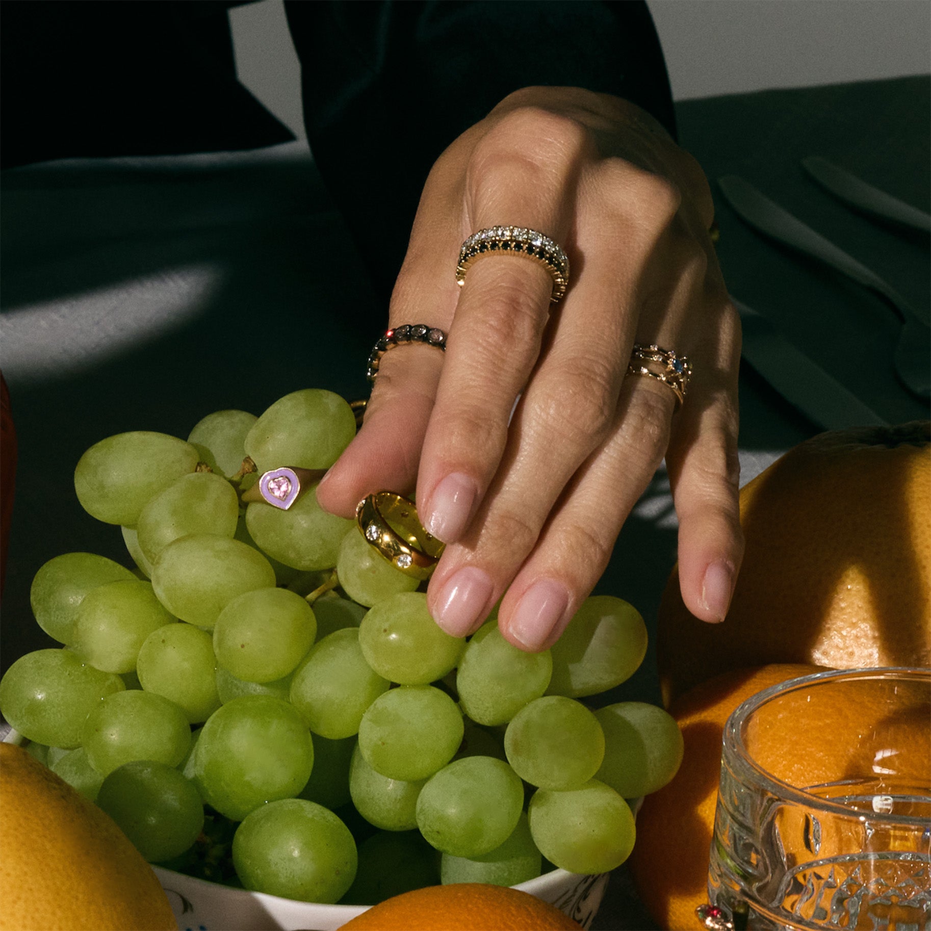 Hand with gorgeous eternity diamond rings on a plate of green grapes and oranges.