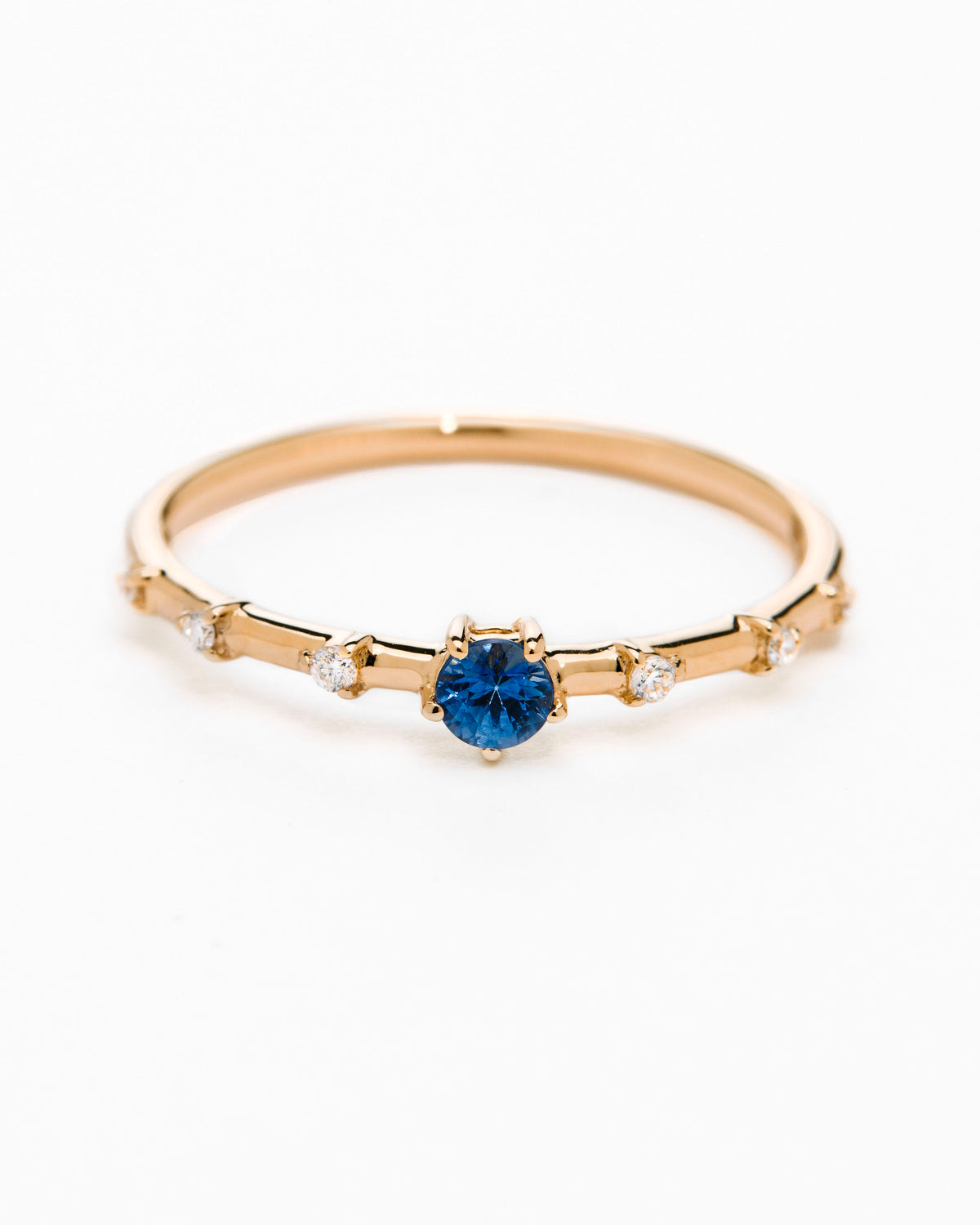A gold band ring featuring a central sapphire with smaller diamond accents around it, presented against a white background.
