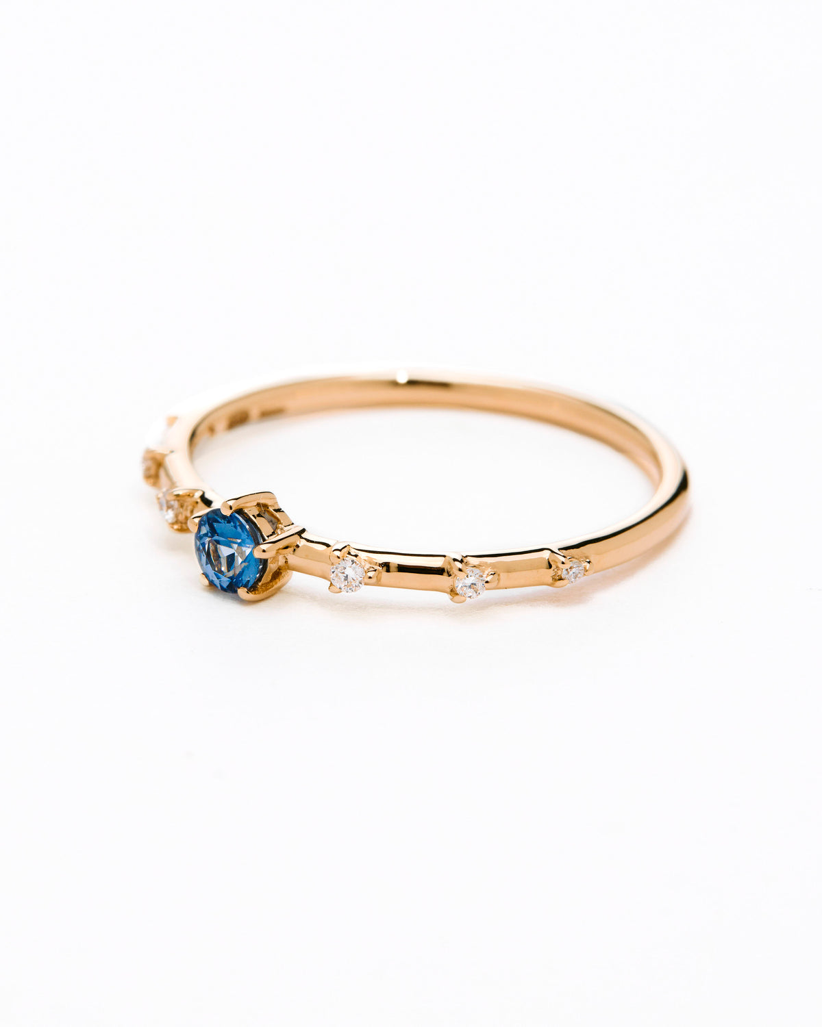 A gold band ring featuring a central sapphire with smaller diamond accents around it, presented against a white background.