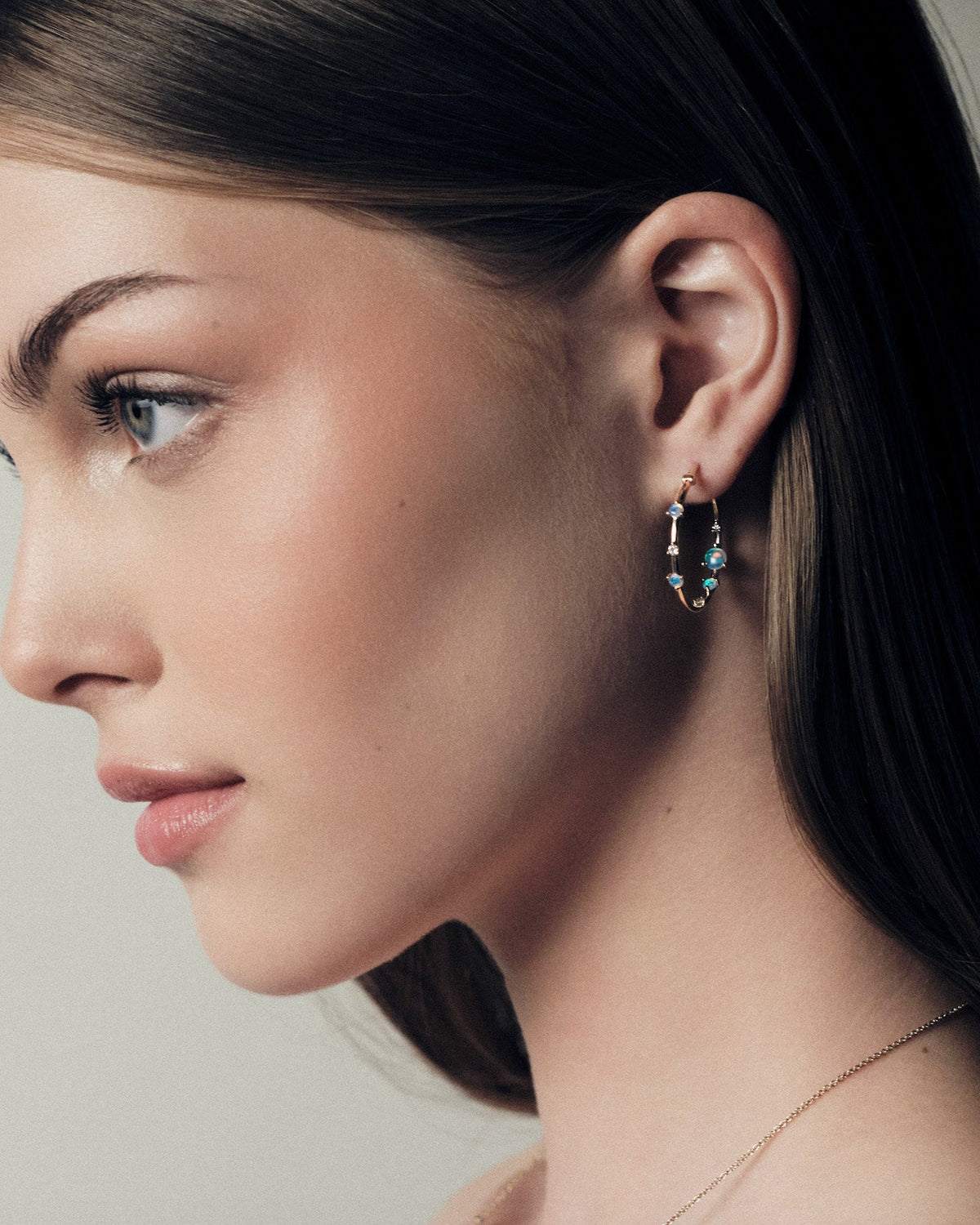 Close-up of a woman wearing australian opals 25mm hoop earrings with a neutral background.