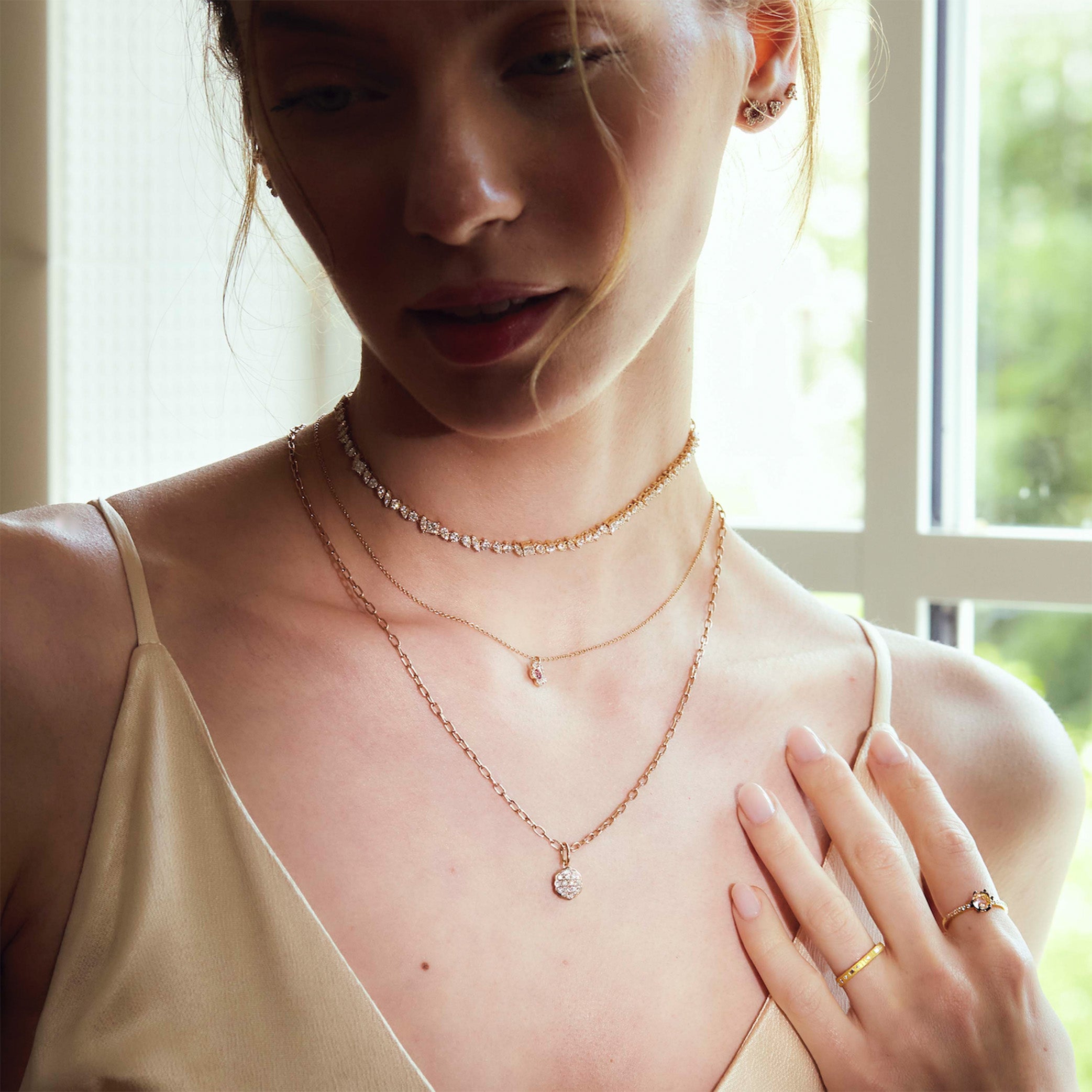 Woman wearing multiple gold and diamonds necklaces and gold and diamonds rings in a softly lit room.