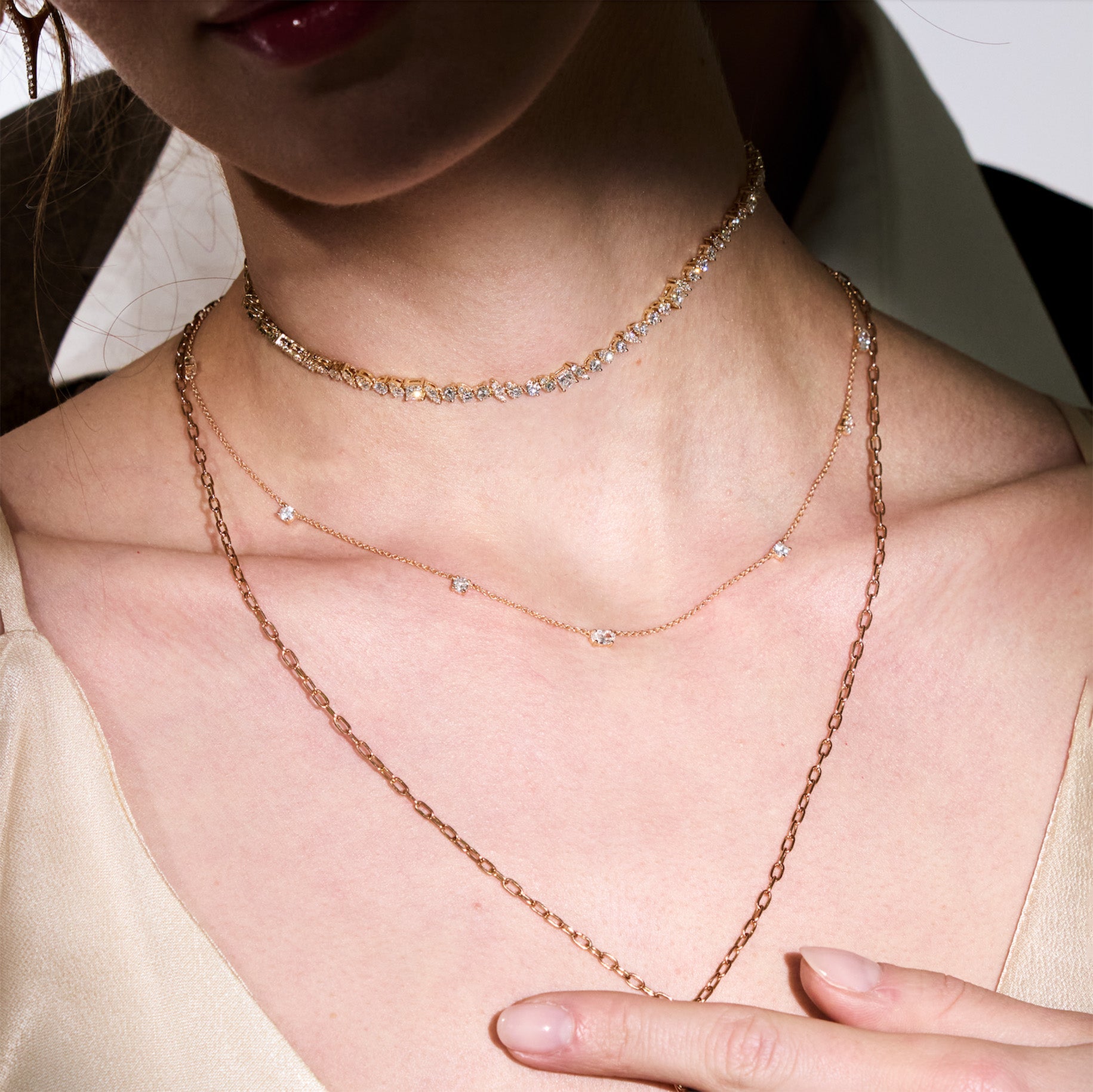 Close-up of a person wearing multiple necklaces, a diamond choker, with a neutral background
