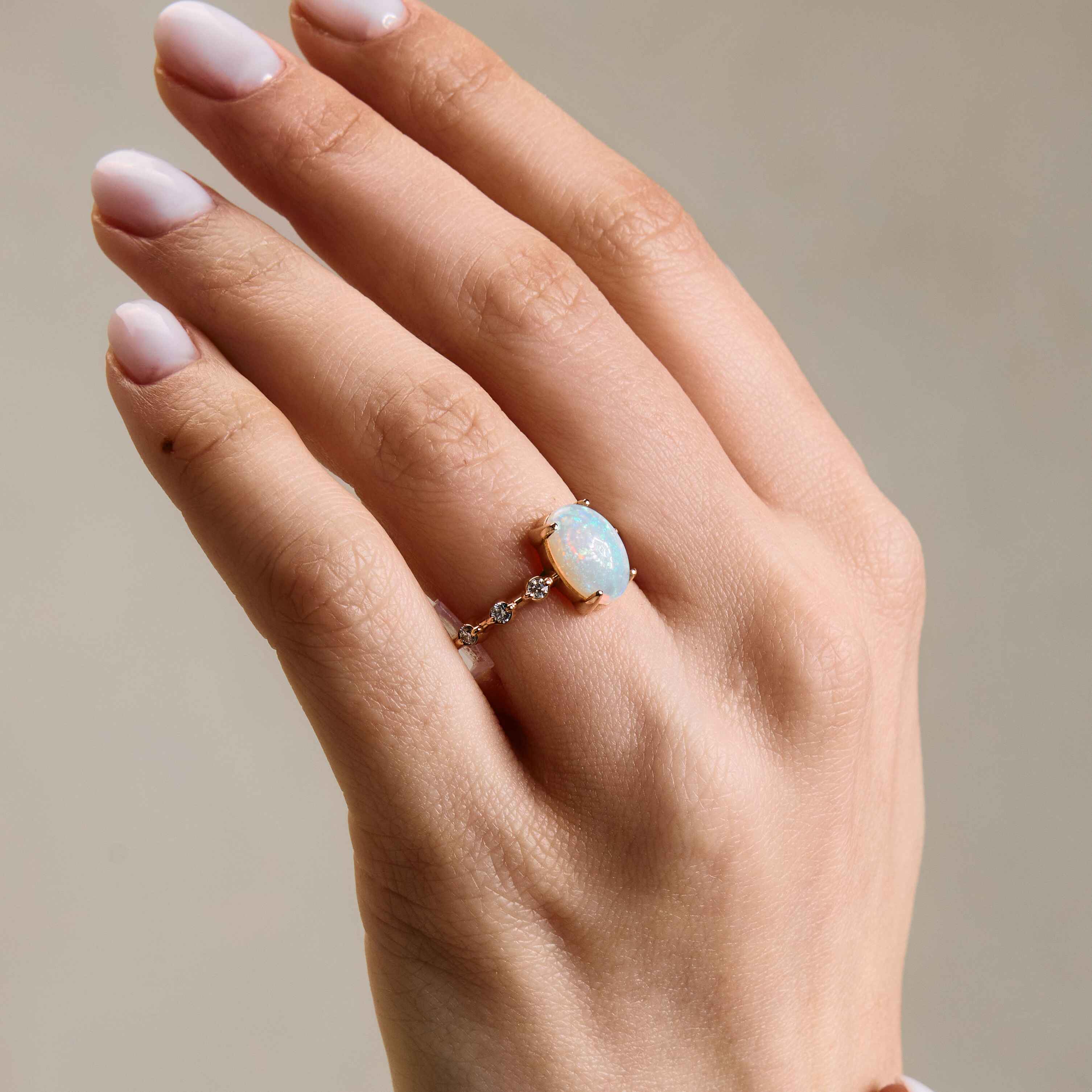 a gold ring with an opal center stone and white diamond accents on the band on hand