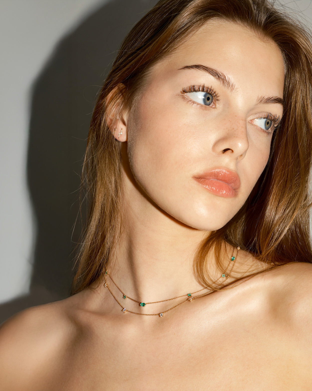 Close-up of a woman wearing gold lightning bolt, and floating dot earrings with diamonds, on a plain background