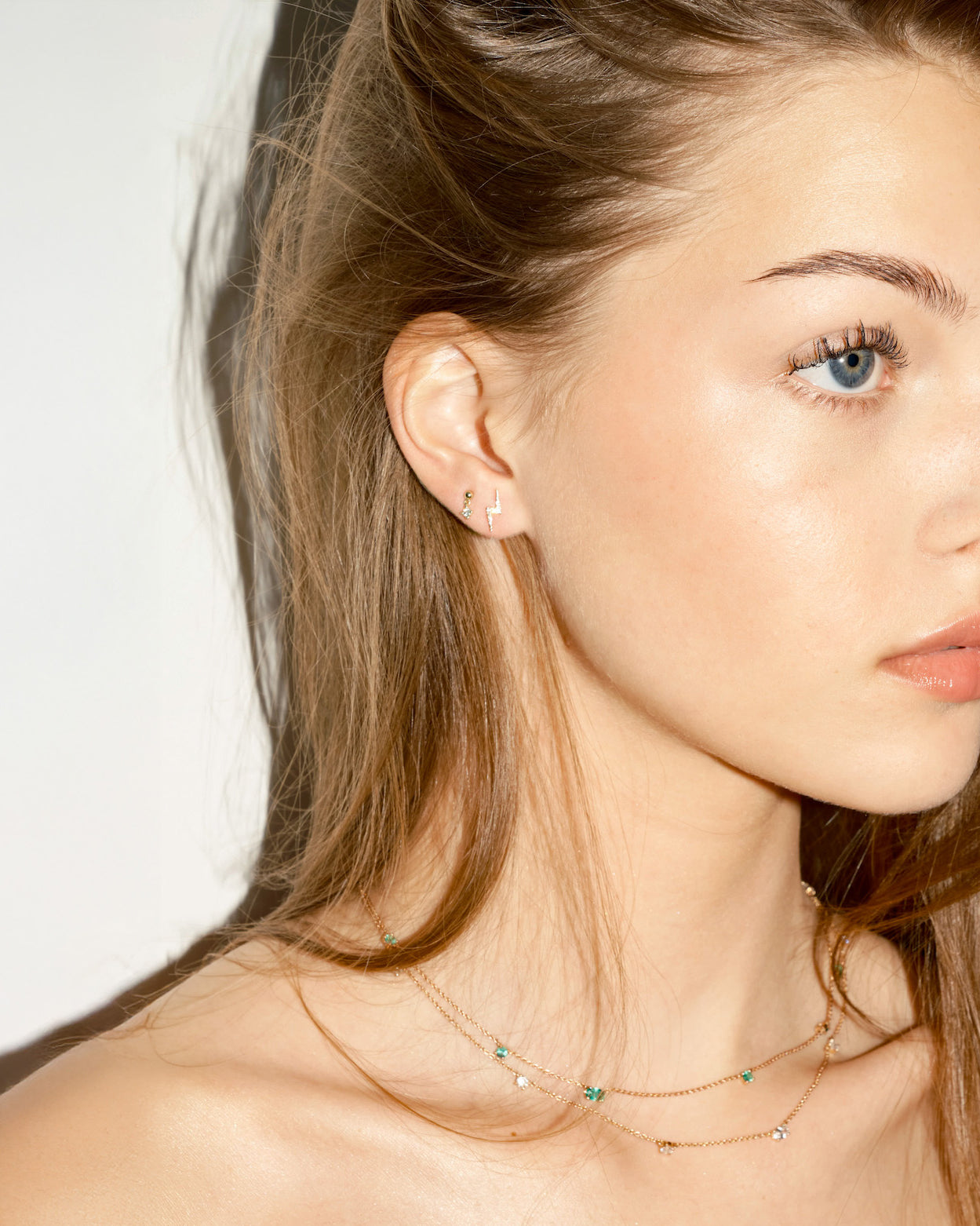 Close-up of a woman wearing a delicate necklace, and old lightning bolt earring with diamonds, on a plain background