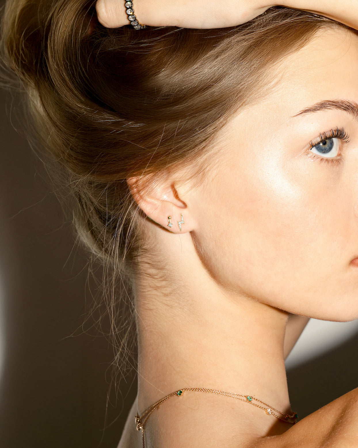 Close-up of a woman wearing gold lightning bolt, and floating dot earrings with diamonds, on a plain background