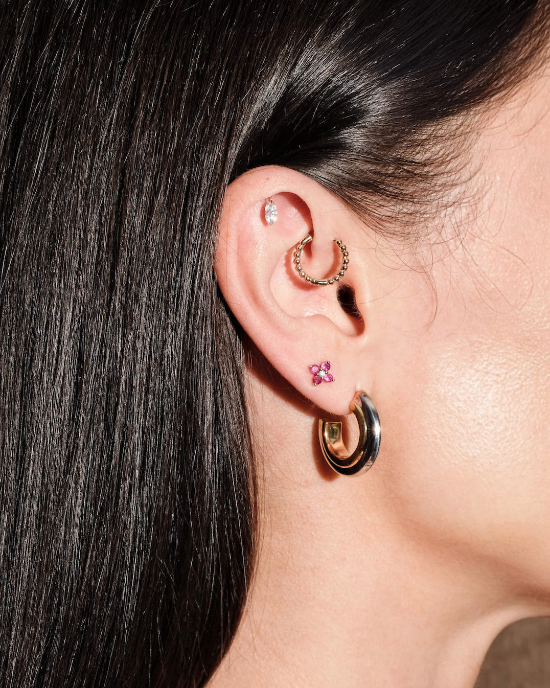 Close-up of an ear with gold hoop earrings, floating marquise diamond earring, and ruby studs on model's ear.