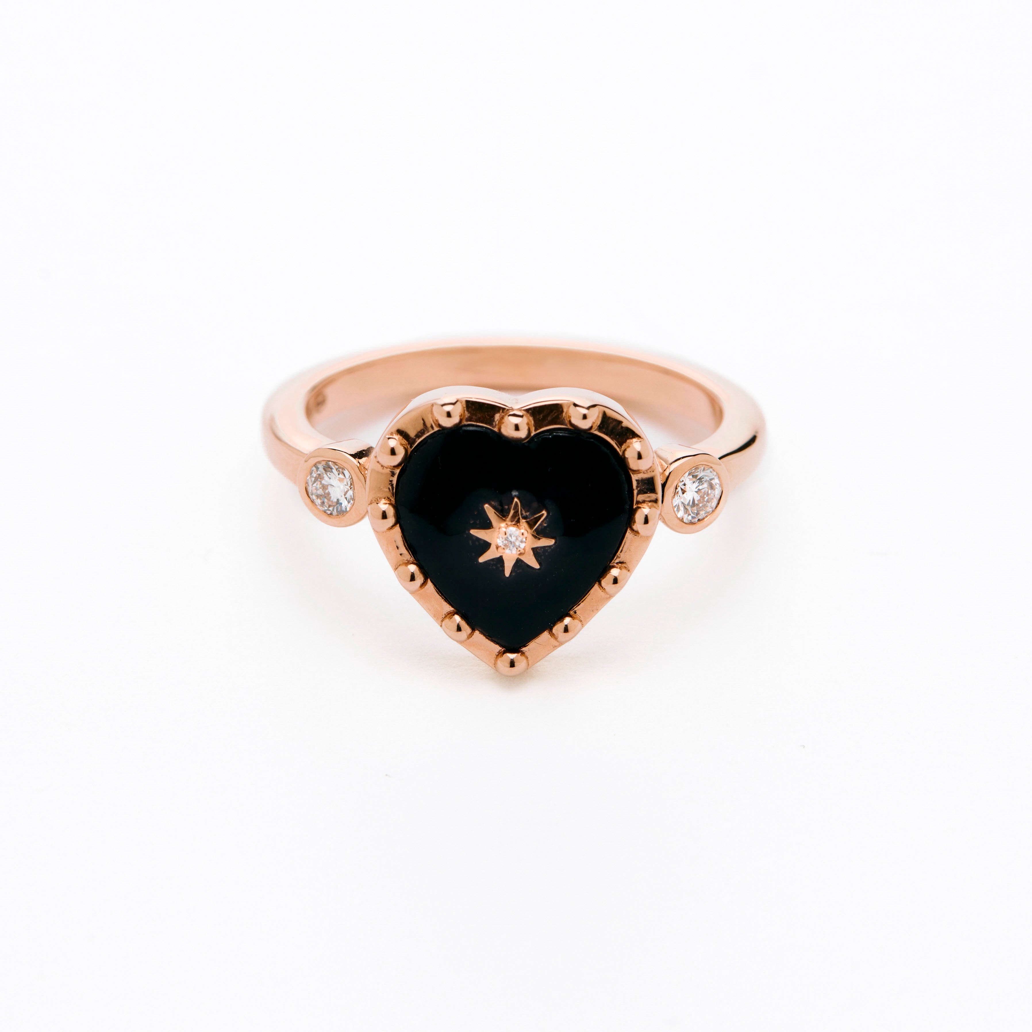 A collection of heart-shaped Black Onyx rings with white diamonds displayed on a white surface with petal decorations.