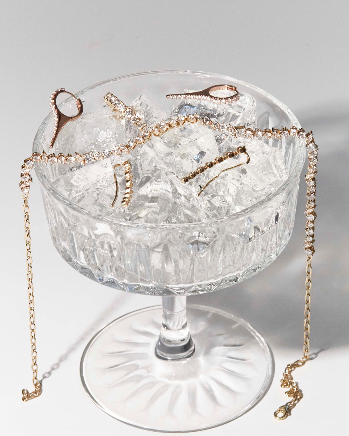A cocktail glass with the perfect brew in it, diamond jewellery of all sorts on ice, earrings, choker and a eternity ring.
Un pahar de cocktail care conține băutura perfectă, bijuterii cu diamante de tot felul, cercei, choker și un inel eternity.
