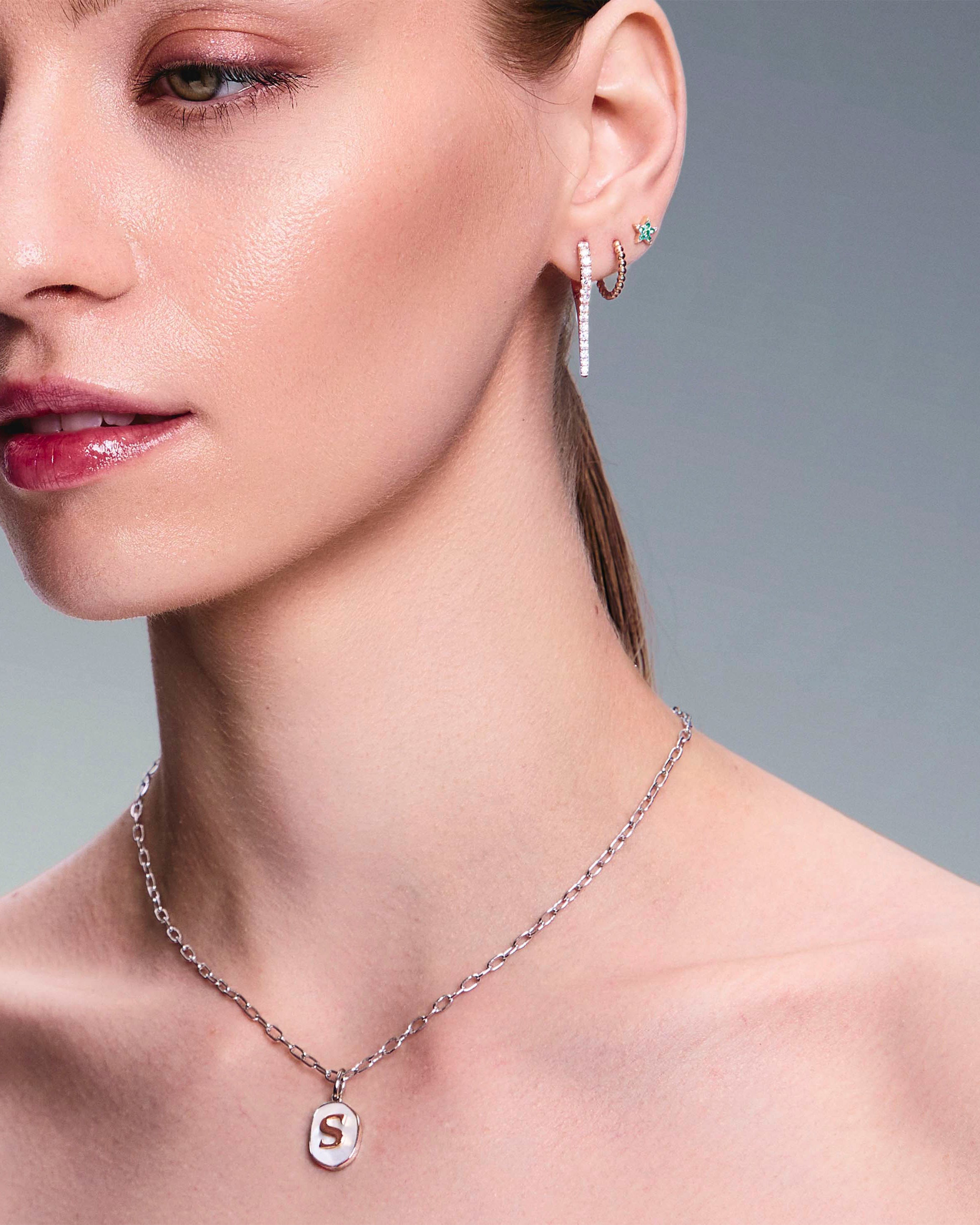 beautiful model wearing a mother of pearl pendant with a gold letter, diamonds drops earrings, gold hoops and star studs earrings.