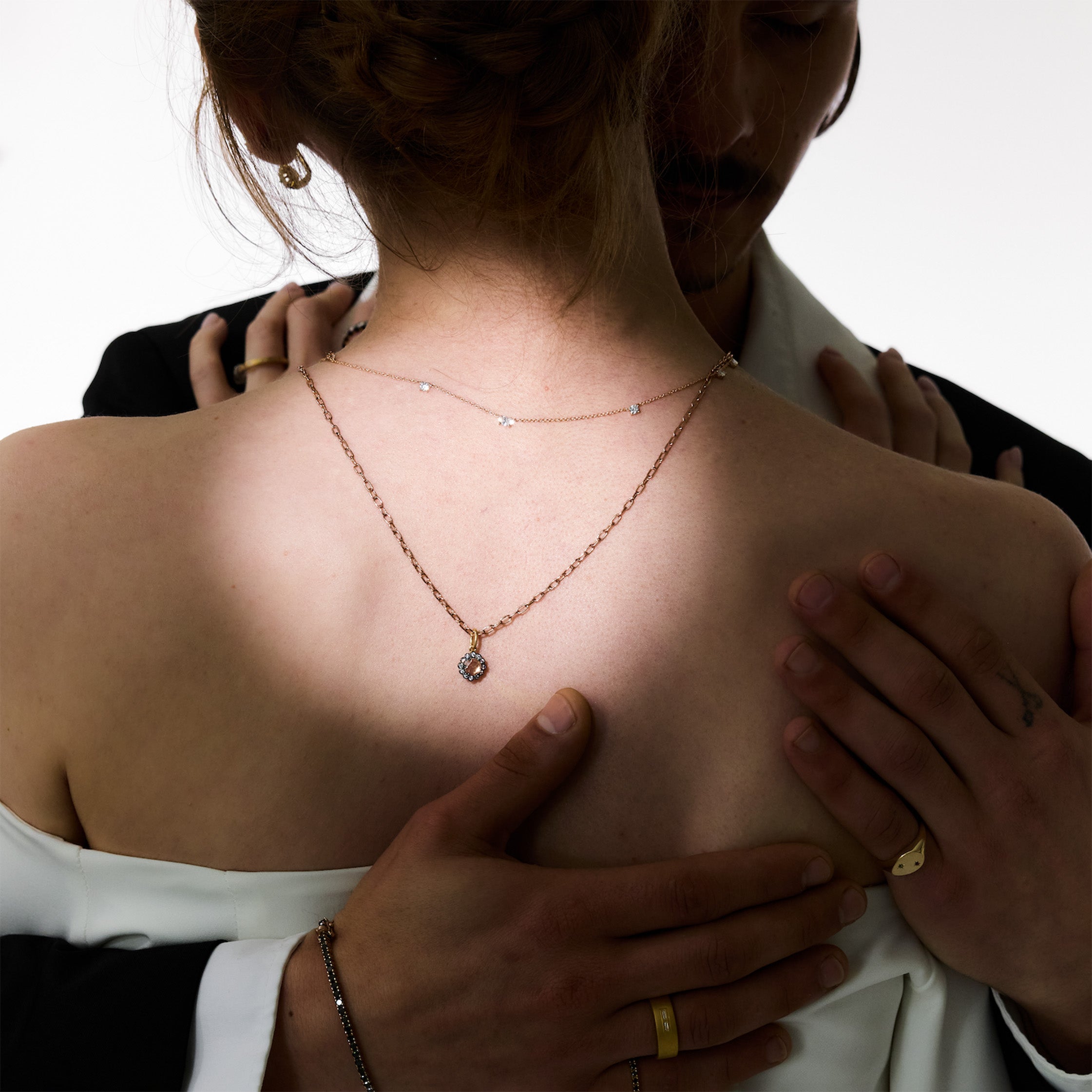 Person wearing a delicate necklace with hands gently holding shoulders