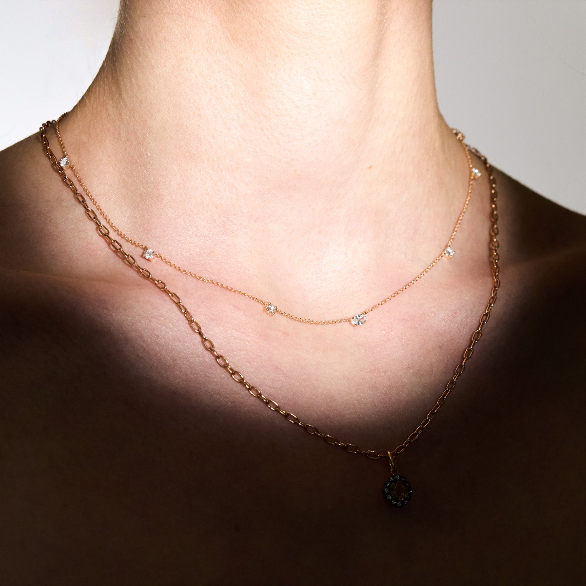 diamonds Necklace and a chain with a pendant on a person's neck against a neutral background