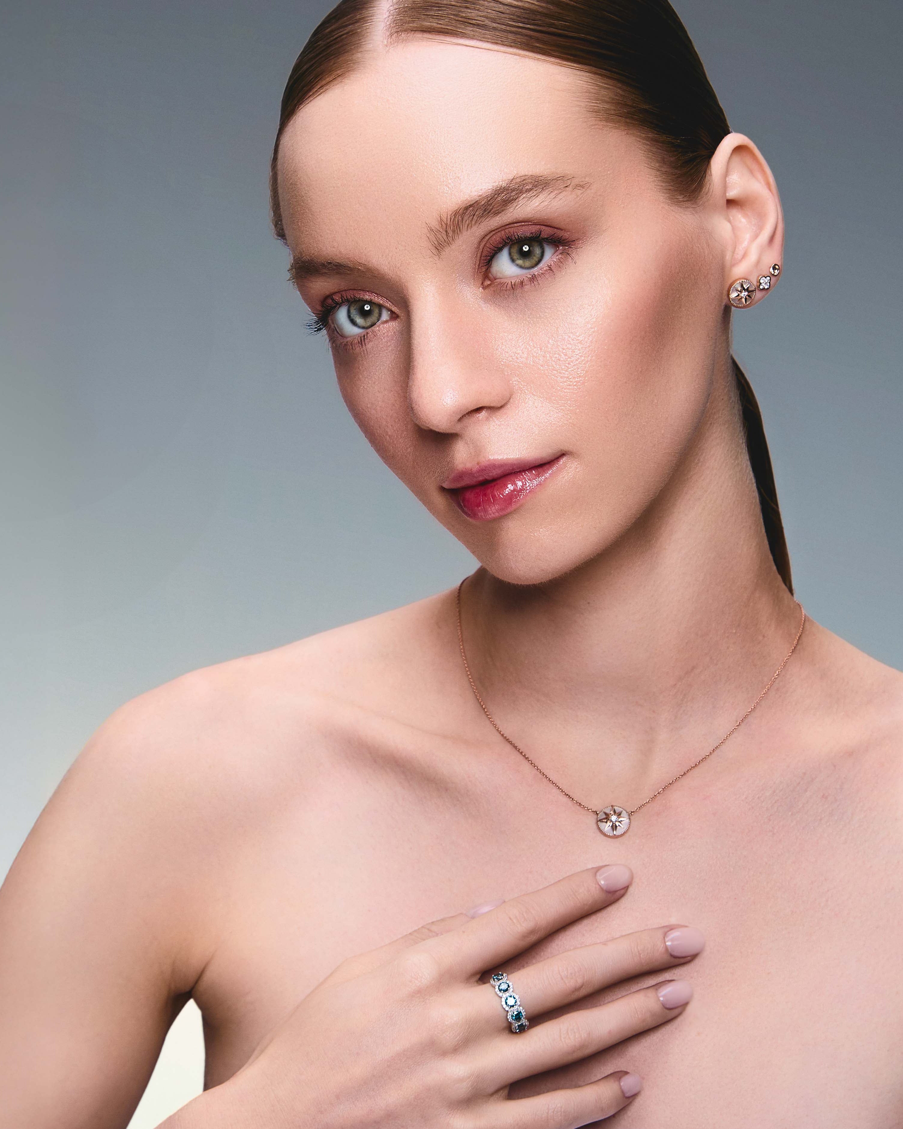 A pair of gold studs earrings with a simple design, resembling a prayer bowl or birds' nest, a clover diamonds earring, a mother of pearl lodestar earring, Lodestar Necklace and blue diamonds half eternity ring on model.