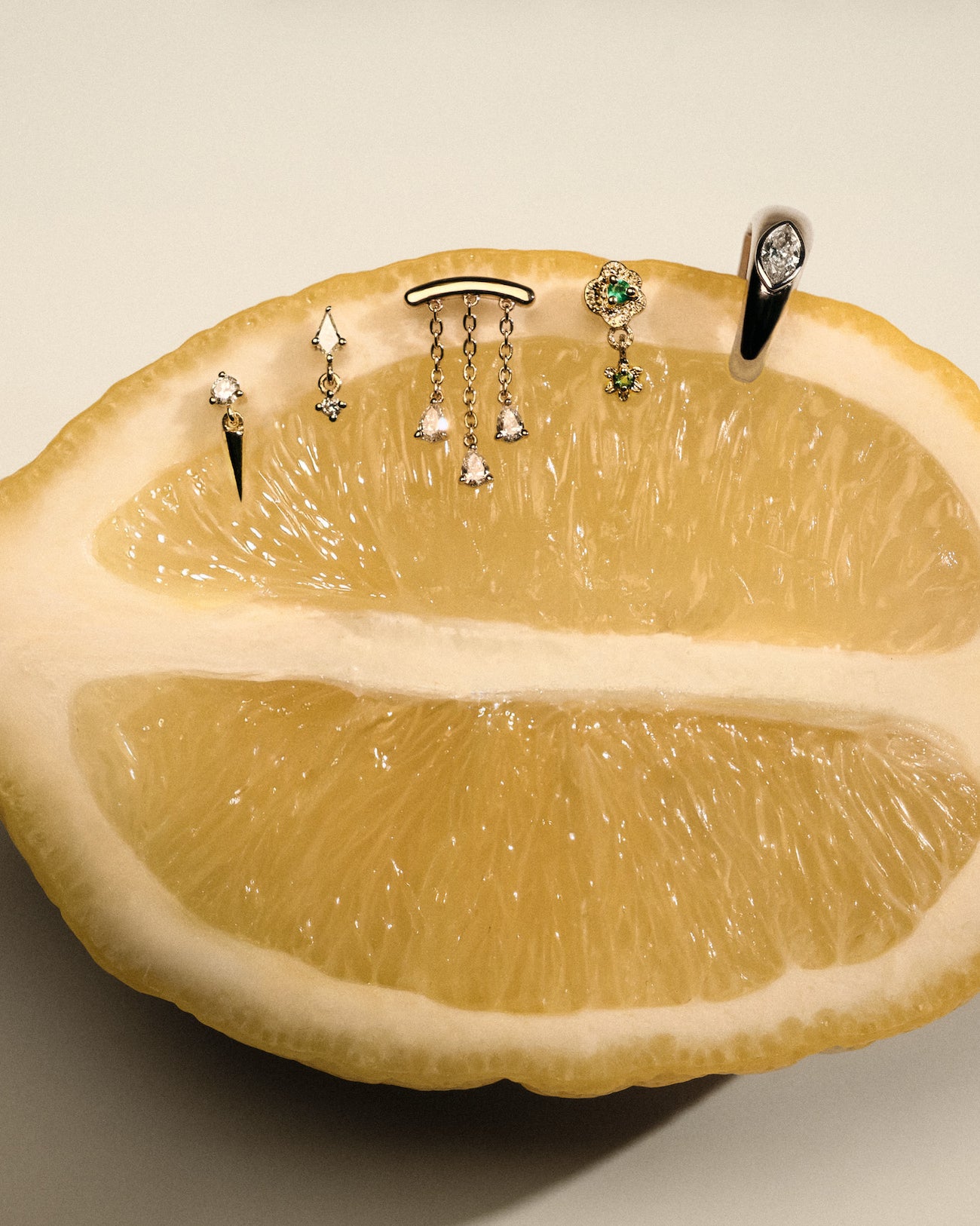 Gold earrings, Teardrop Diamonds Chandelier stud, The Floating Kite Diamond Stud, The Floating Gold Icicle Stud, The Marquise Earcuff, The Wild Rose Stud with Emerald on a lemon with a neutral backgrounda.