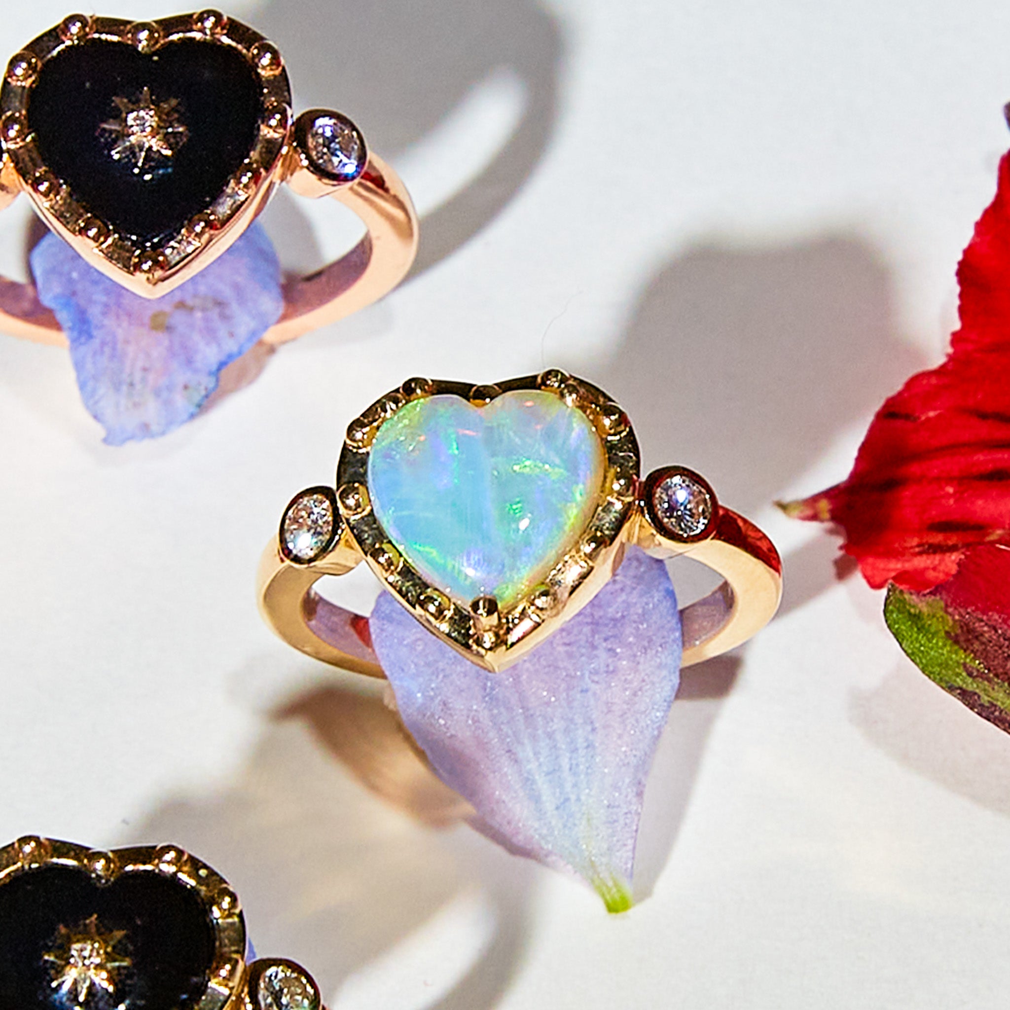 A custom Australian Opal and Diamonds ring with a heart-shaped center stone and round diamond accents, set in a gold band, displayed on a floral surface.