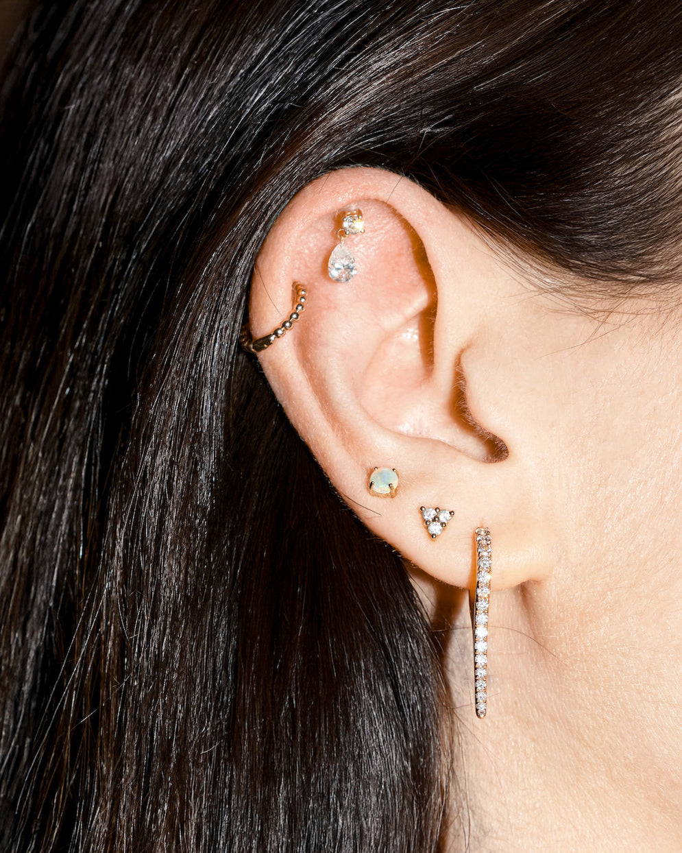 Close-up of an ear with multiple gold and diamonds earrings against a neutral background