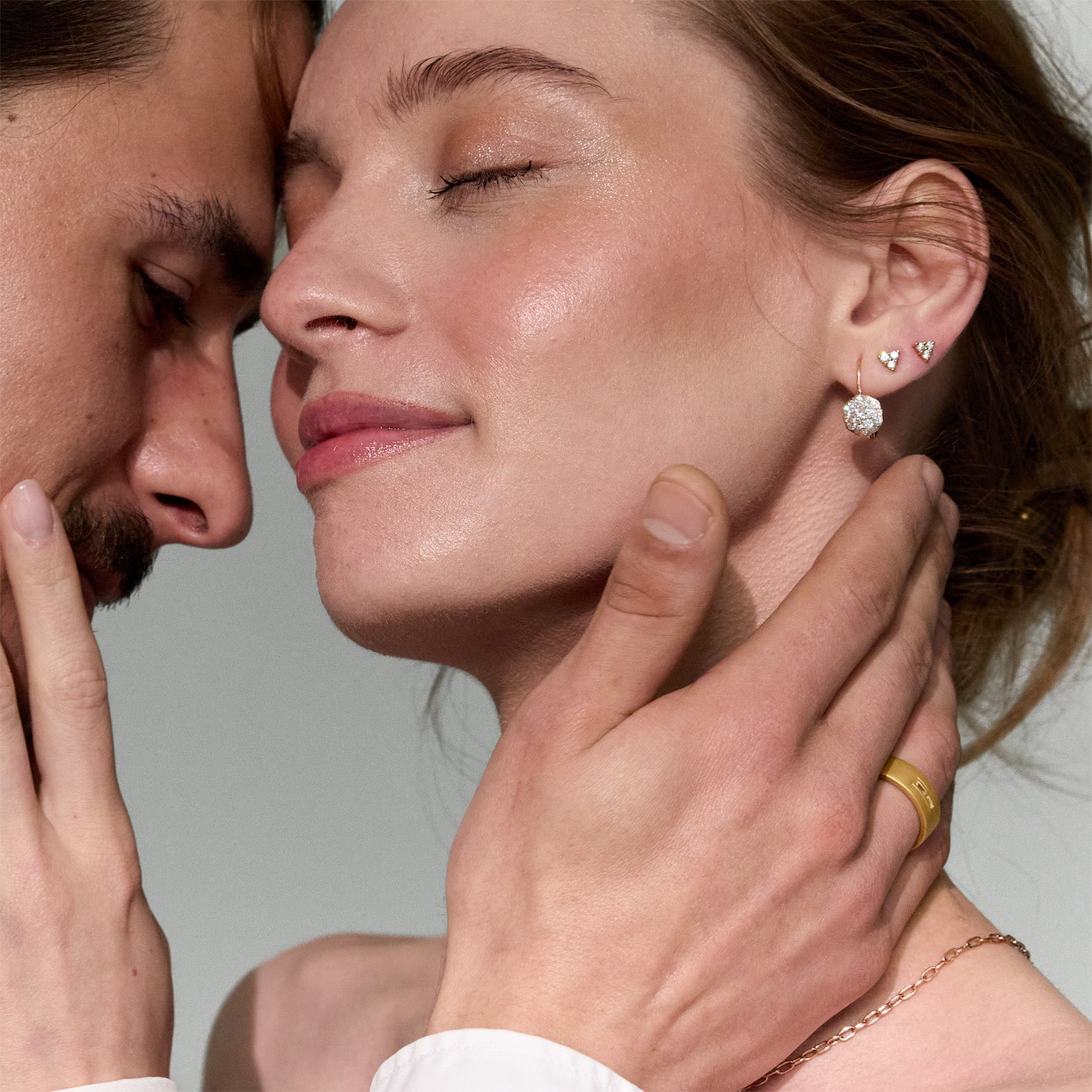 Close-up of a couple having an intimate moment, with a focus on gold and diamonds jewelry, including earrings and a wedding band ring.