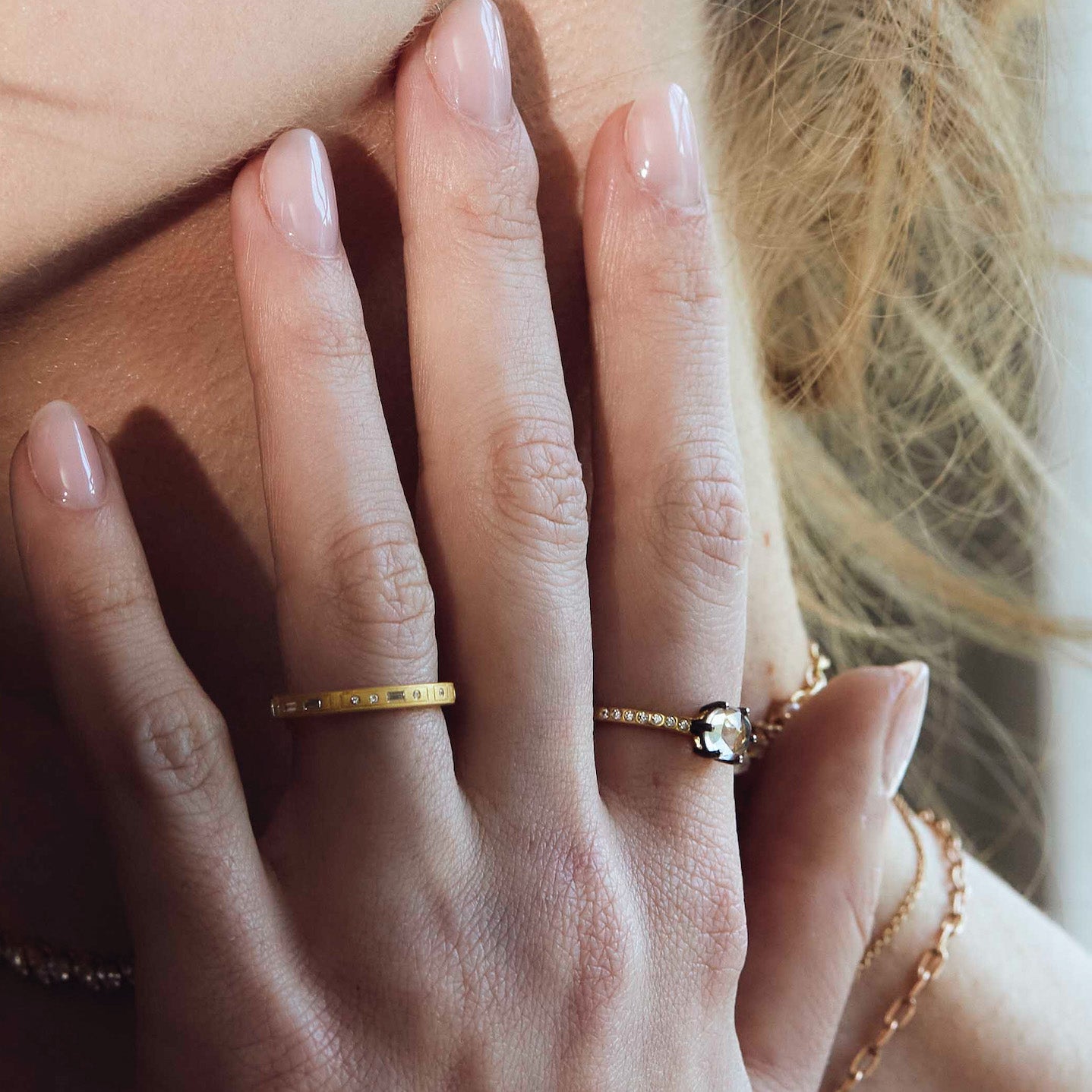 Close-up of a hand wearing two gold rings with diamonds with a blurred background