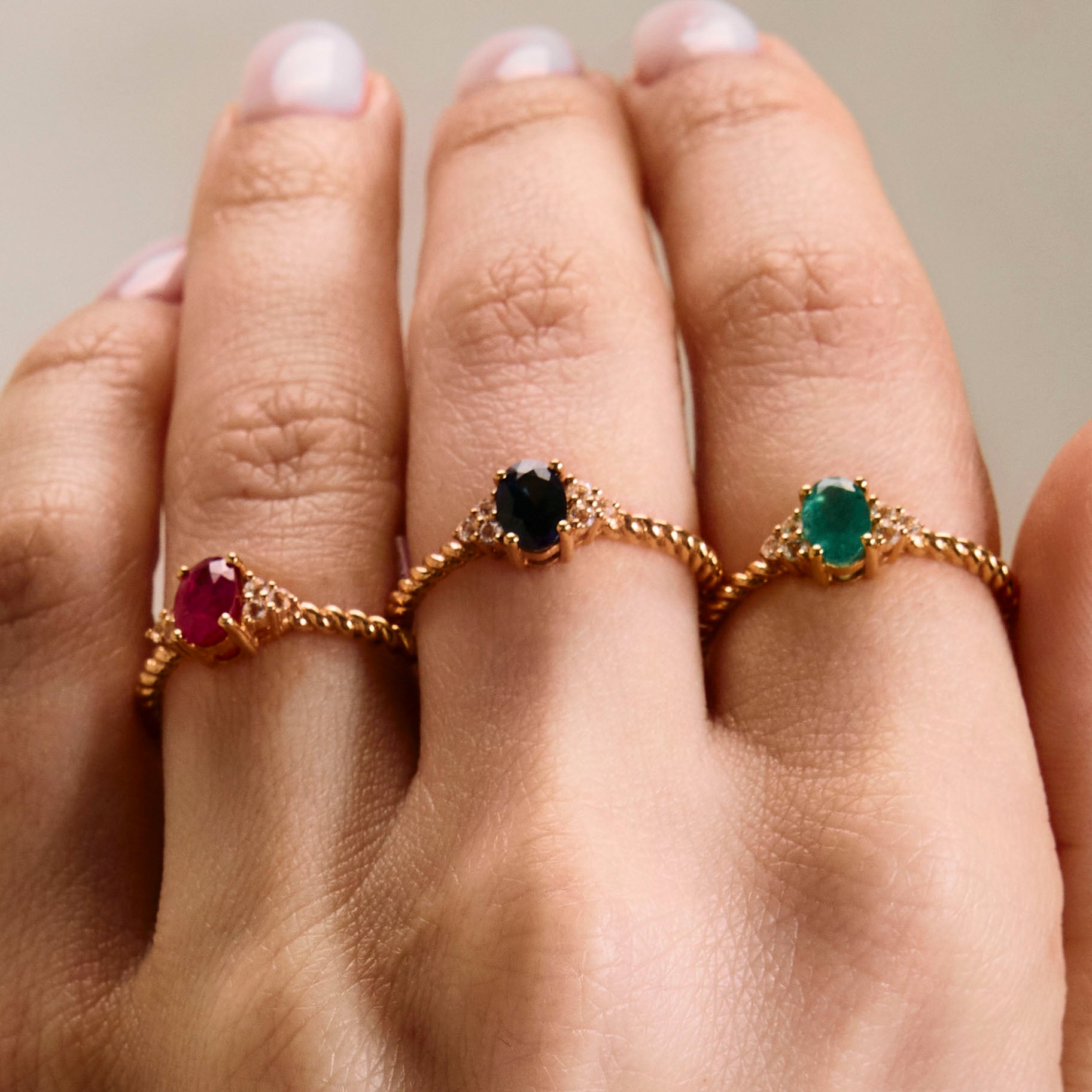 elegant oval blue sapphire ring, oval ruby ring and oval emerald ring with diamonds side cluster and a twisted band on hand