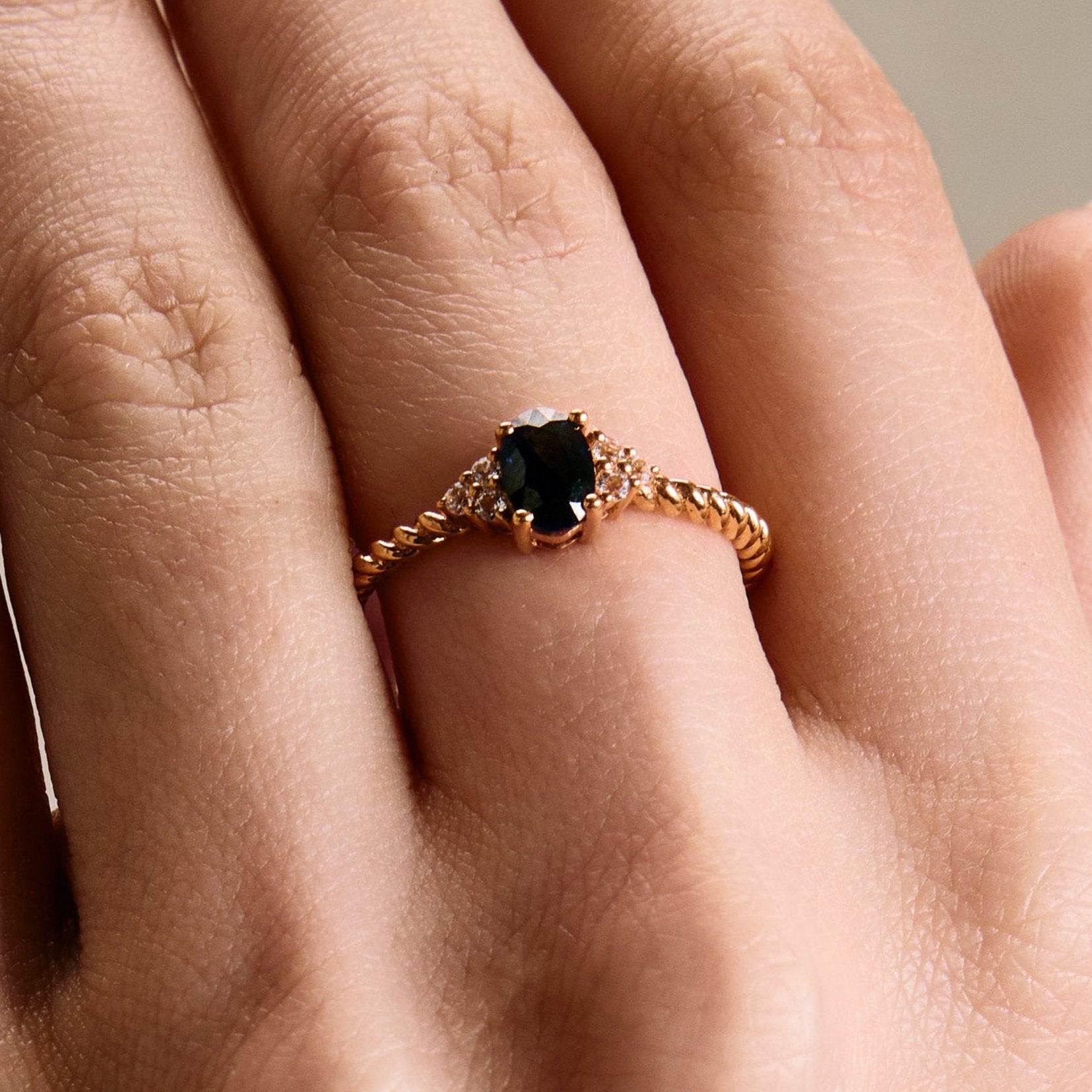 elegant oval blue sapphire ring with diamonds side cluster and a twisted band on hand