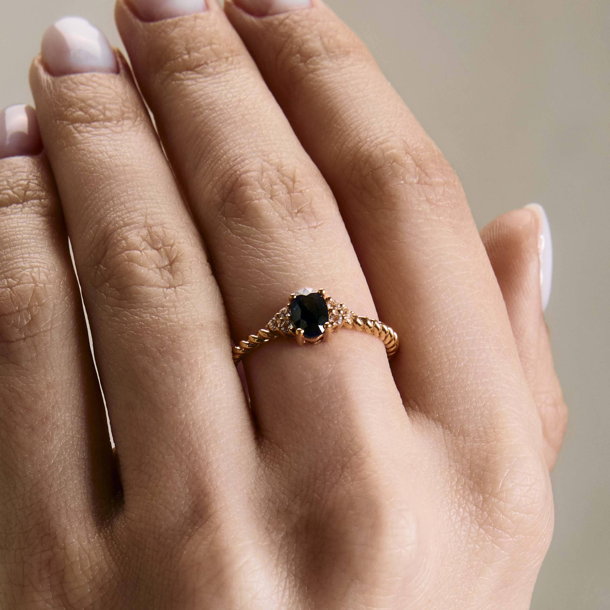 elegant oval blue sapphire ring with diamonds side cluster and a twisted band on hand