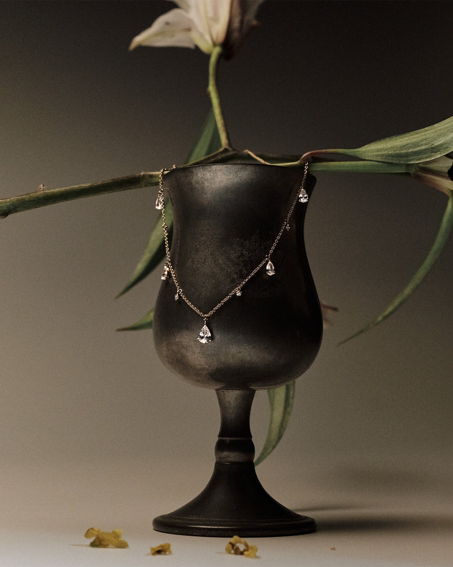 Gold Necklace with teardrop and round diamonds pendants on a black stand with green leaves in the background.