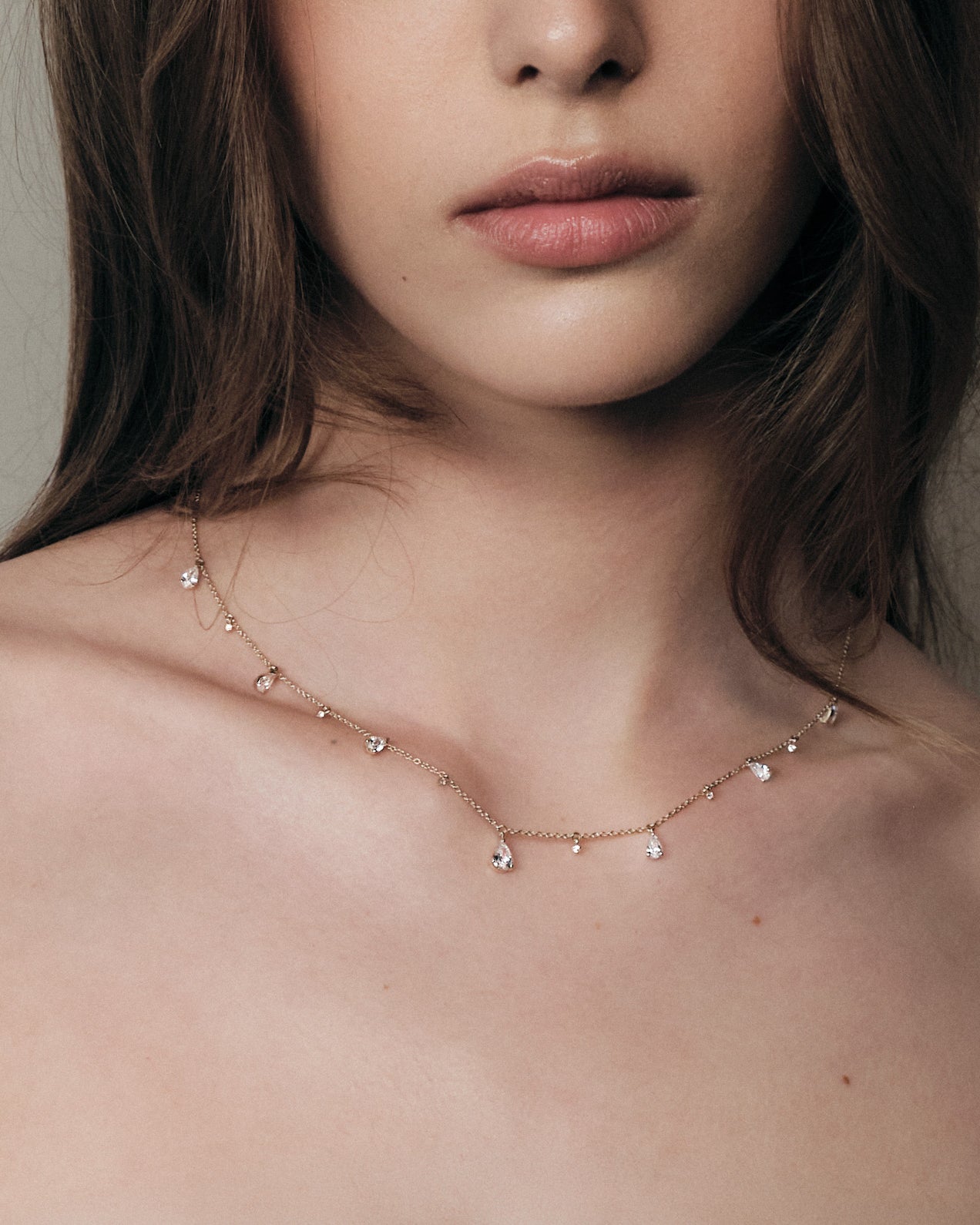 Close-up of a woman wearing a delicate teardrop diamonds necklace with a neutral background.